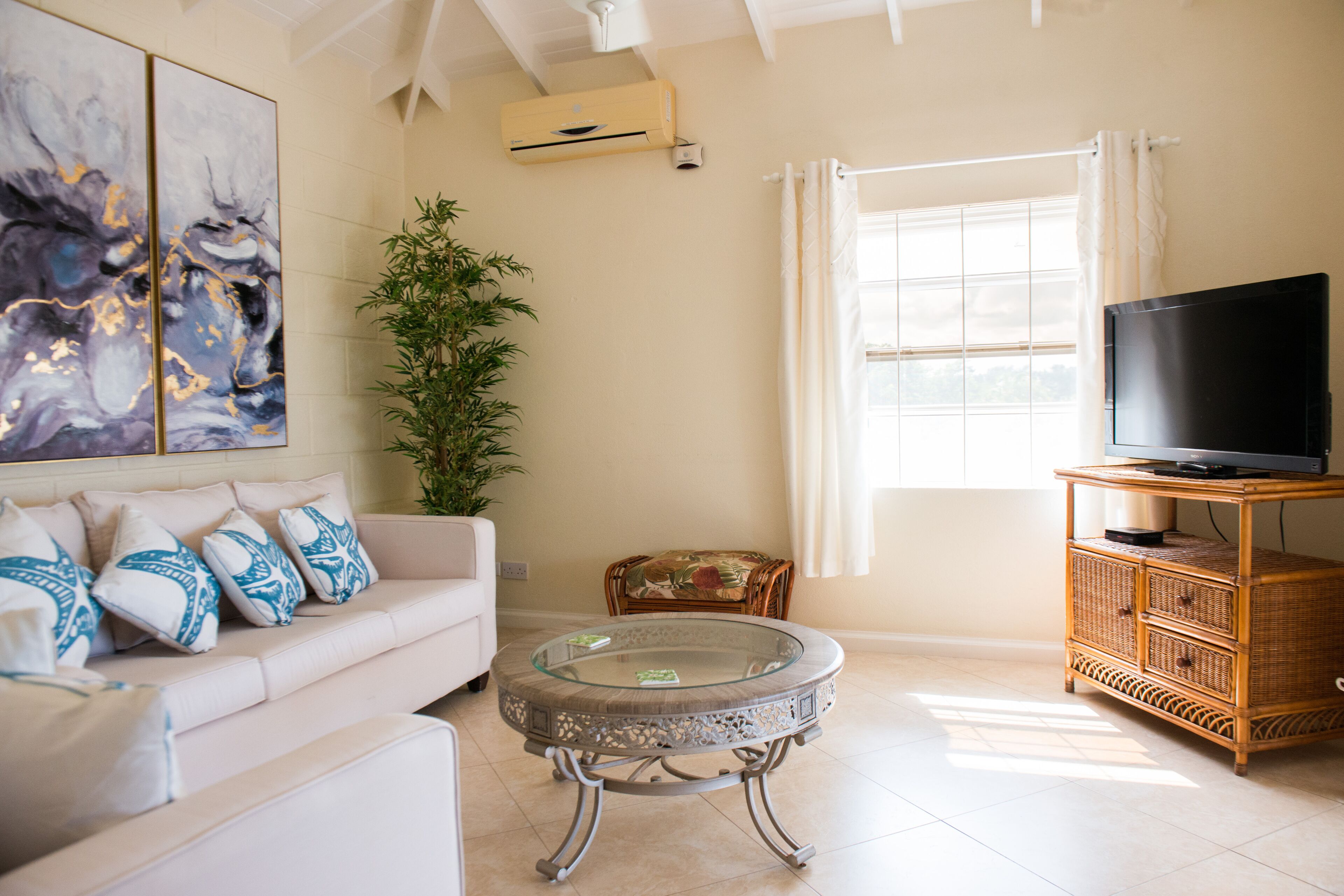The living room has a cream sofa, a television, and a rattan cabinet.