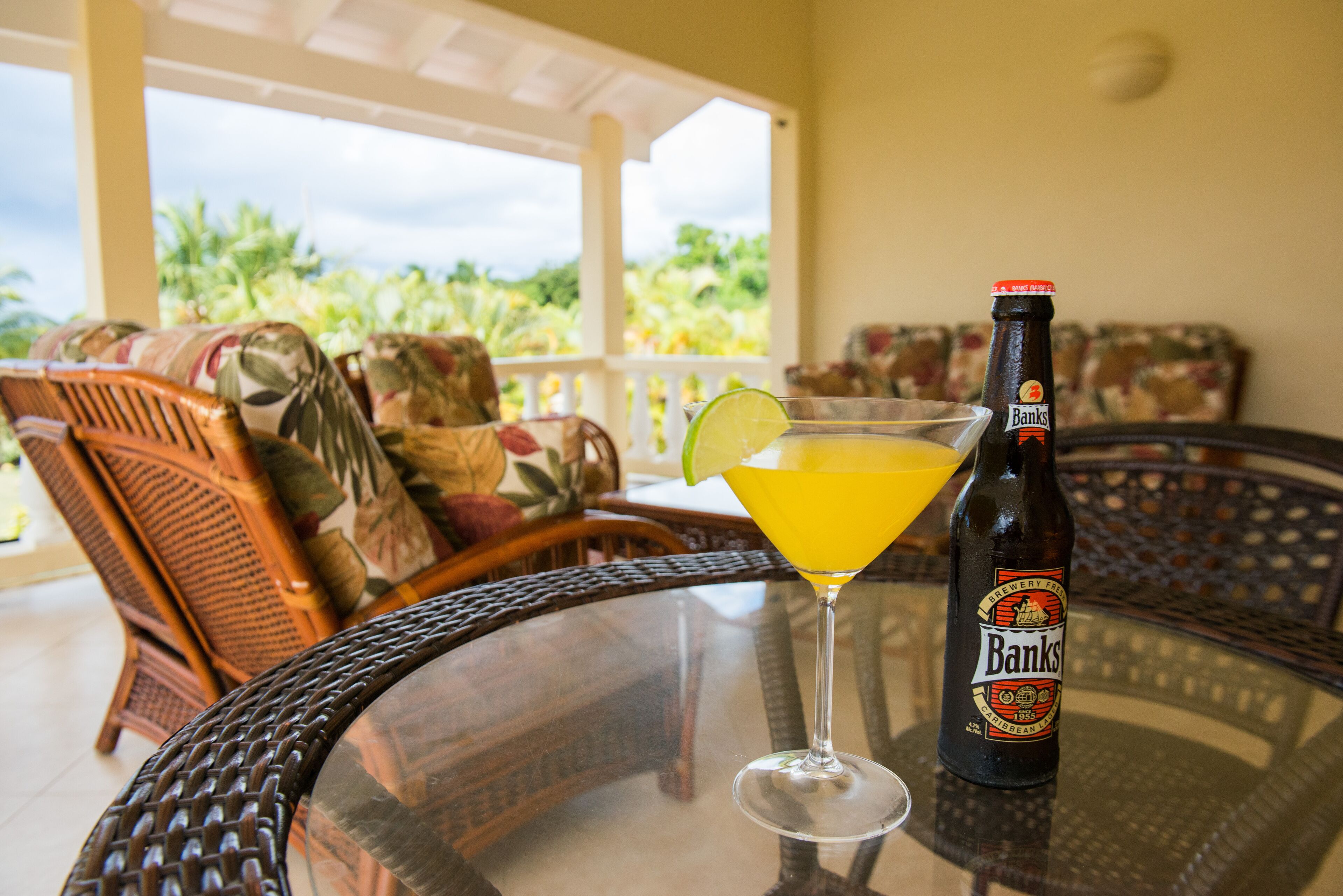 A cocktail and a bottle of beer stand on a glass table on the veranda.