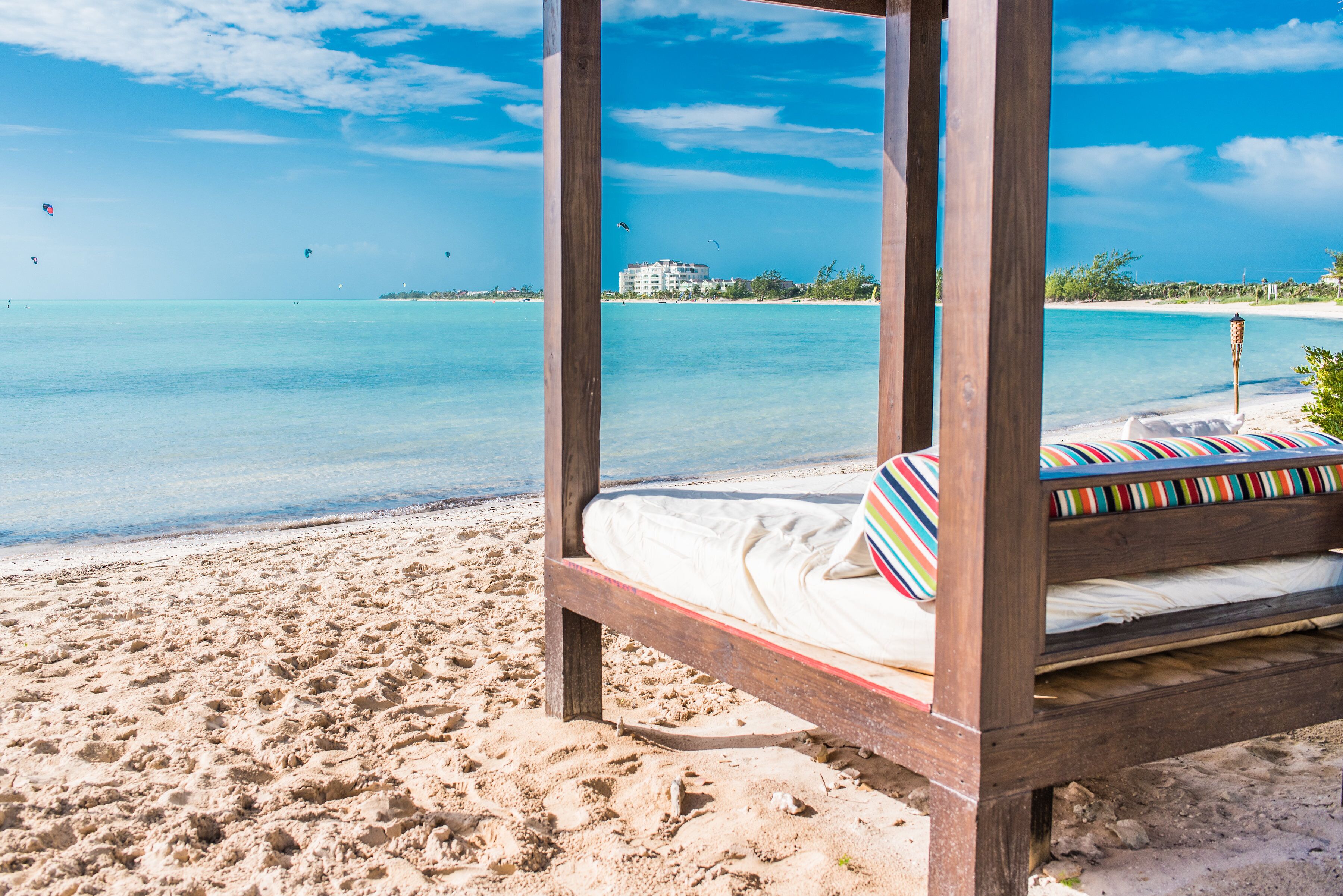 A canopy daybed on the sand with the sea behind it.