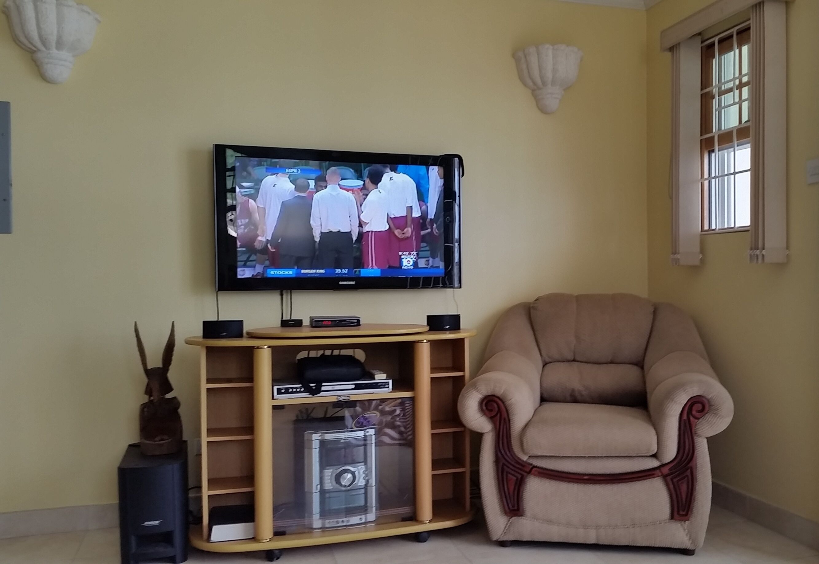 The living room with a television on the wall and an armchair.