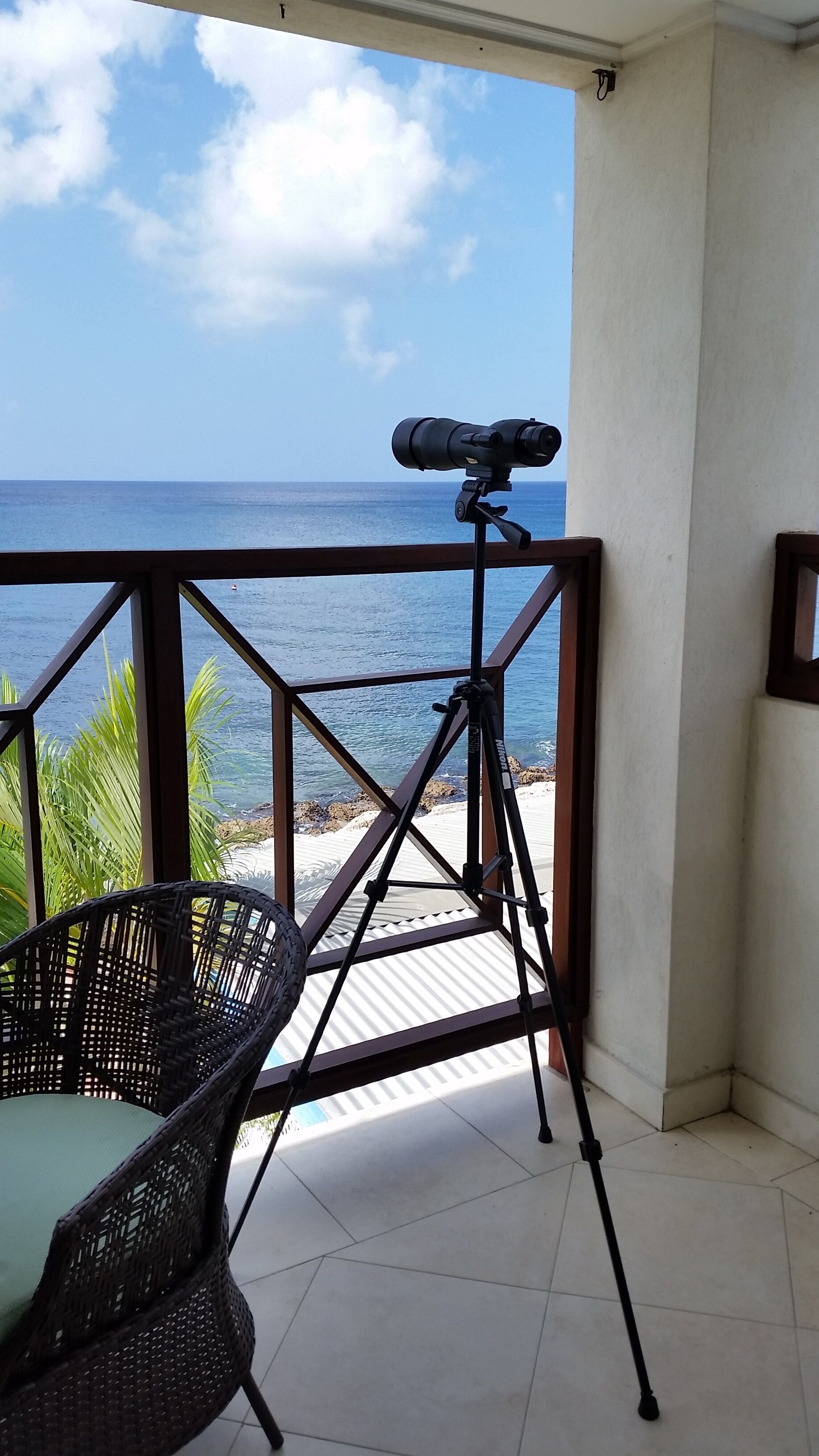 A spotting scope on a tripod on the balcony, with a view of the sea.