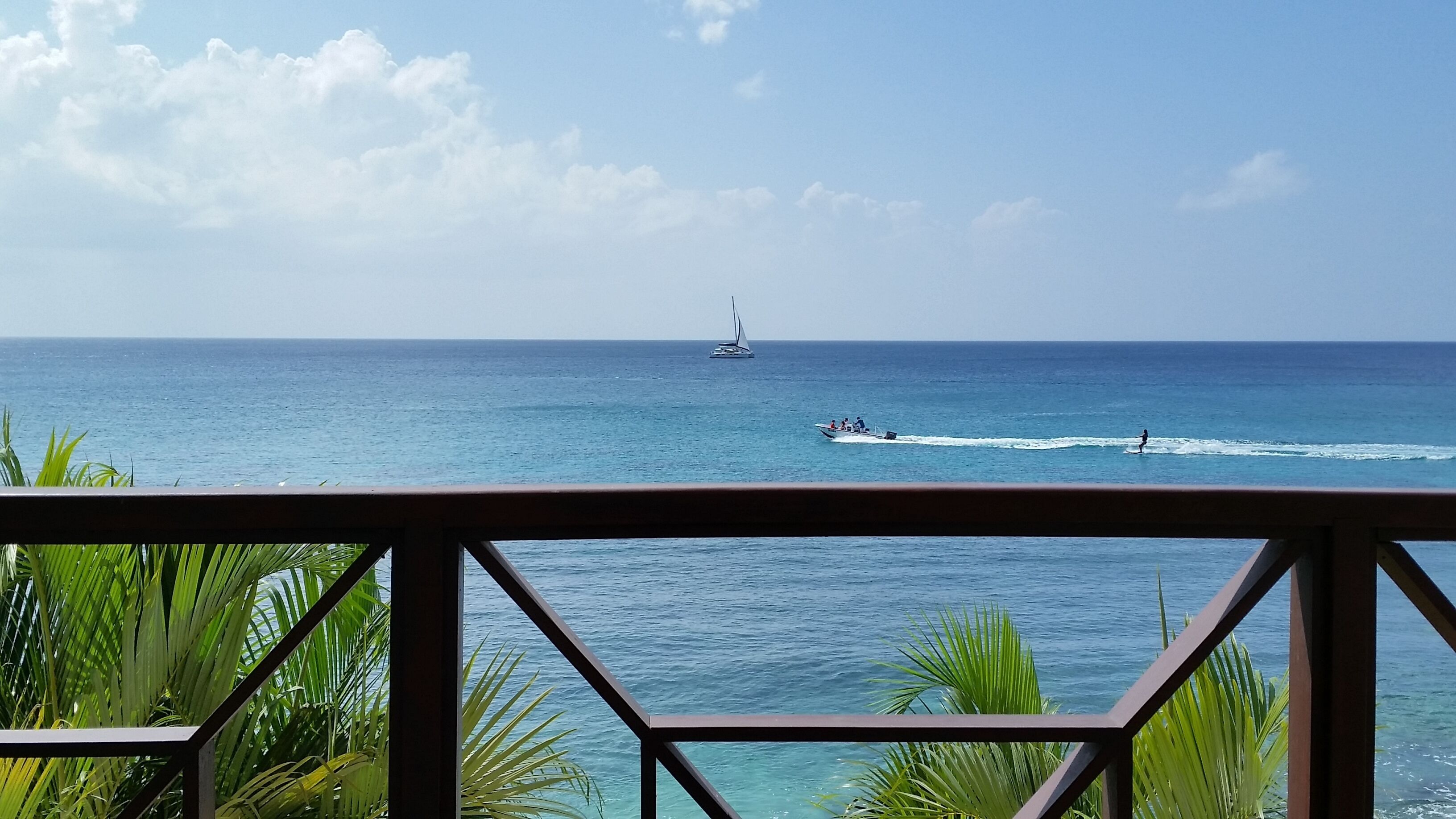 A view of the sea from the balcony, with a sailboat and a speedboat.