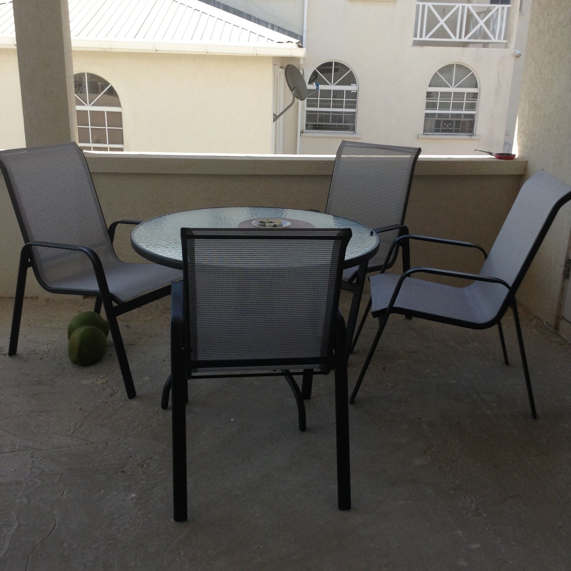 A covered patio with a round glass table and four chairs.