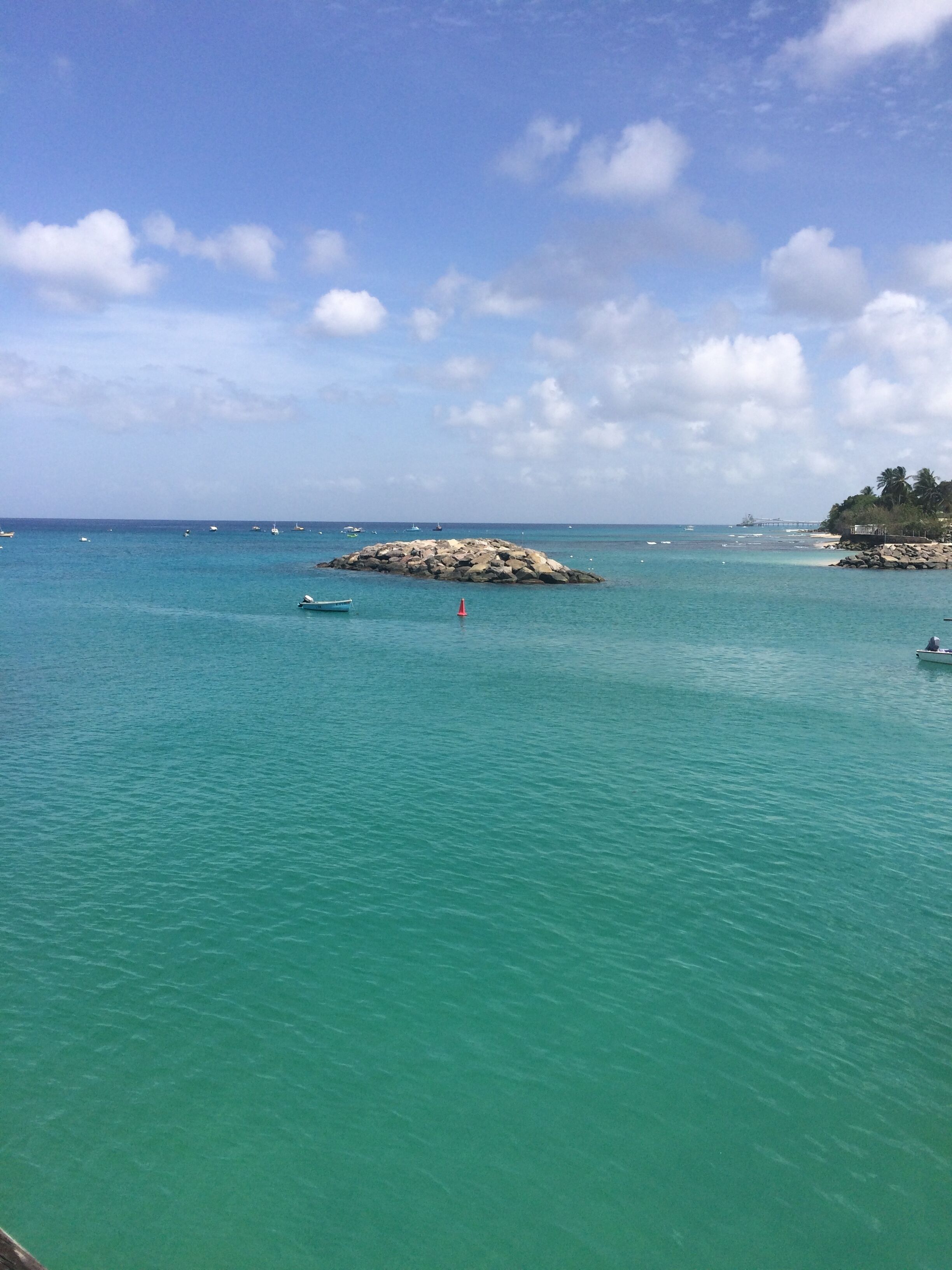 A view of the sea with boats and a stone breakwater.
