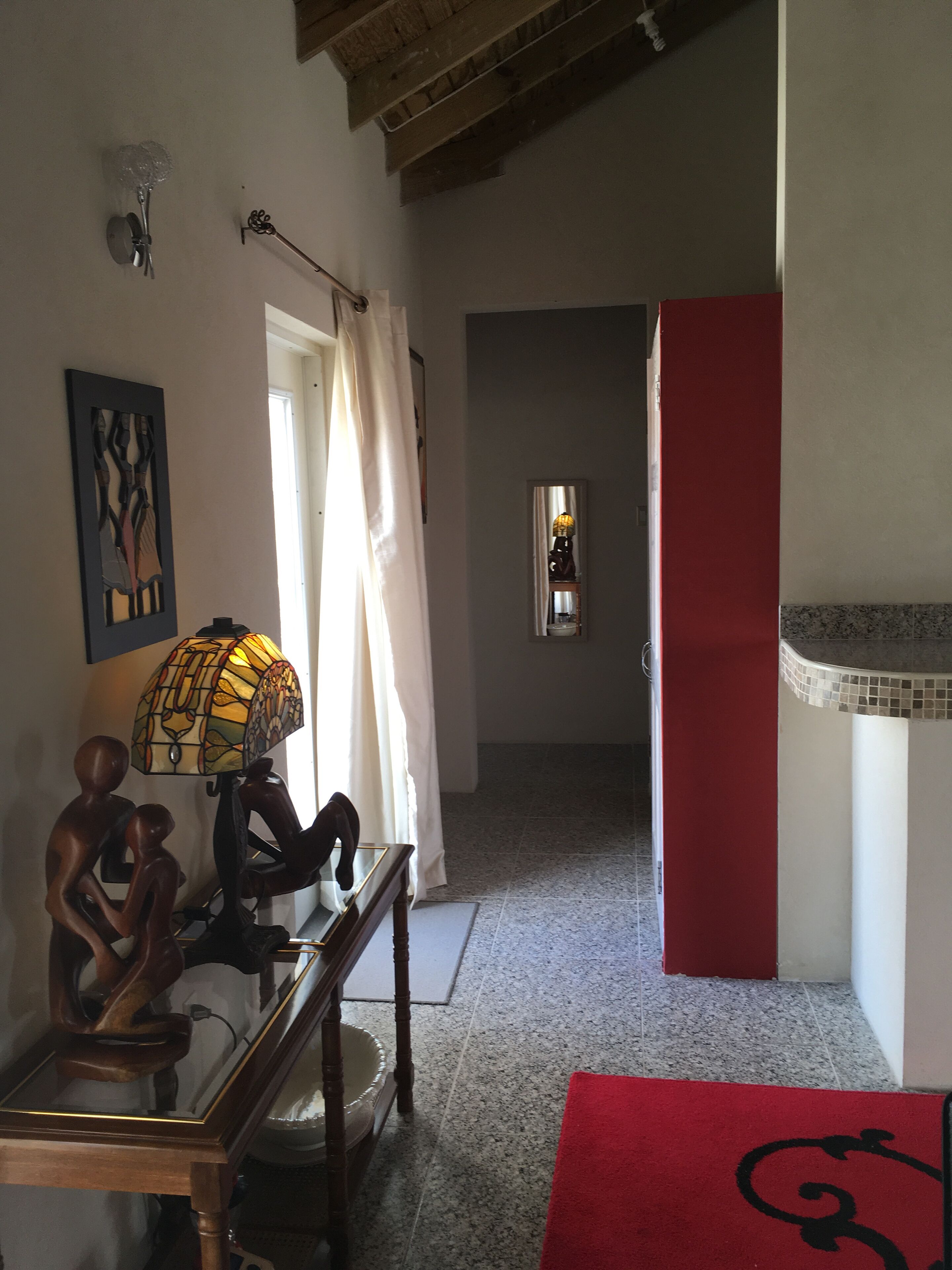A hallway with a console table, a lamp, and wood carvings.