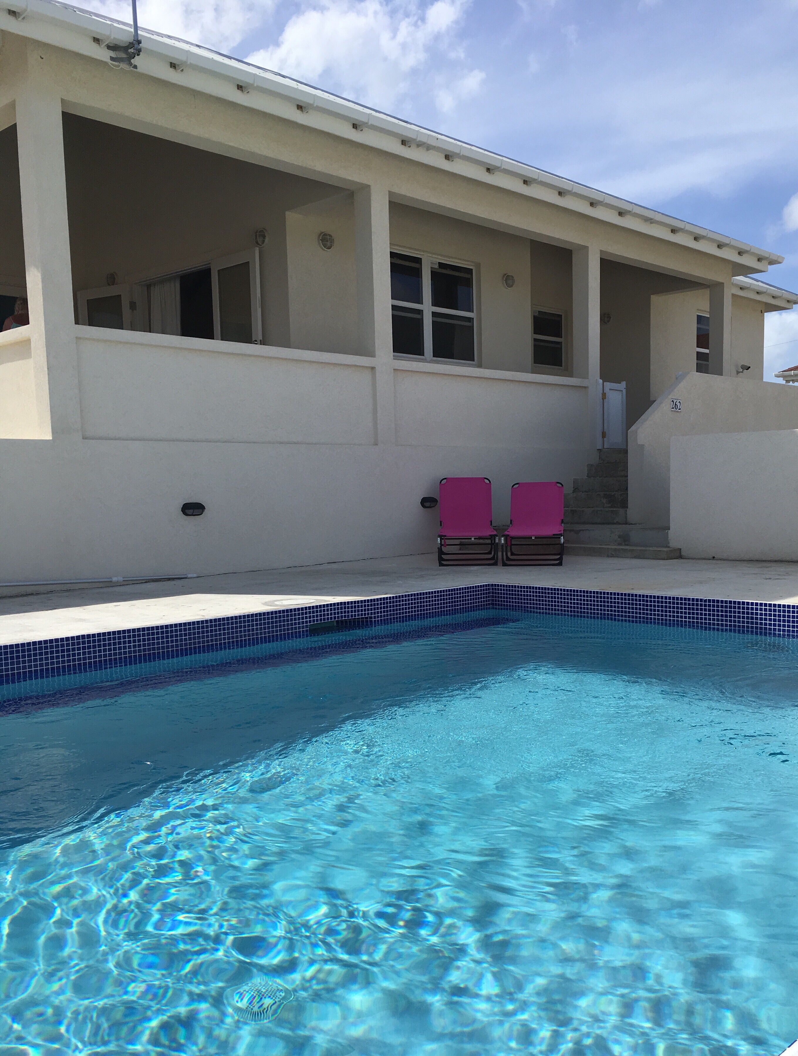 The pool with two pink chairs in front of the villa.