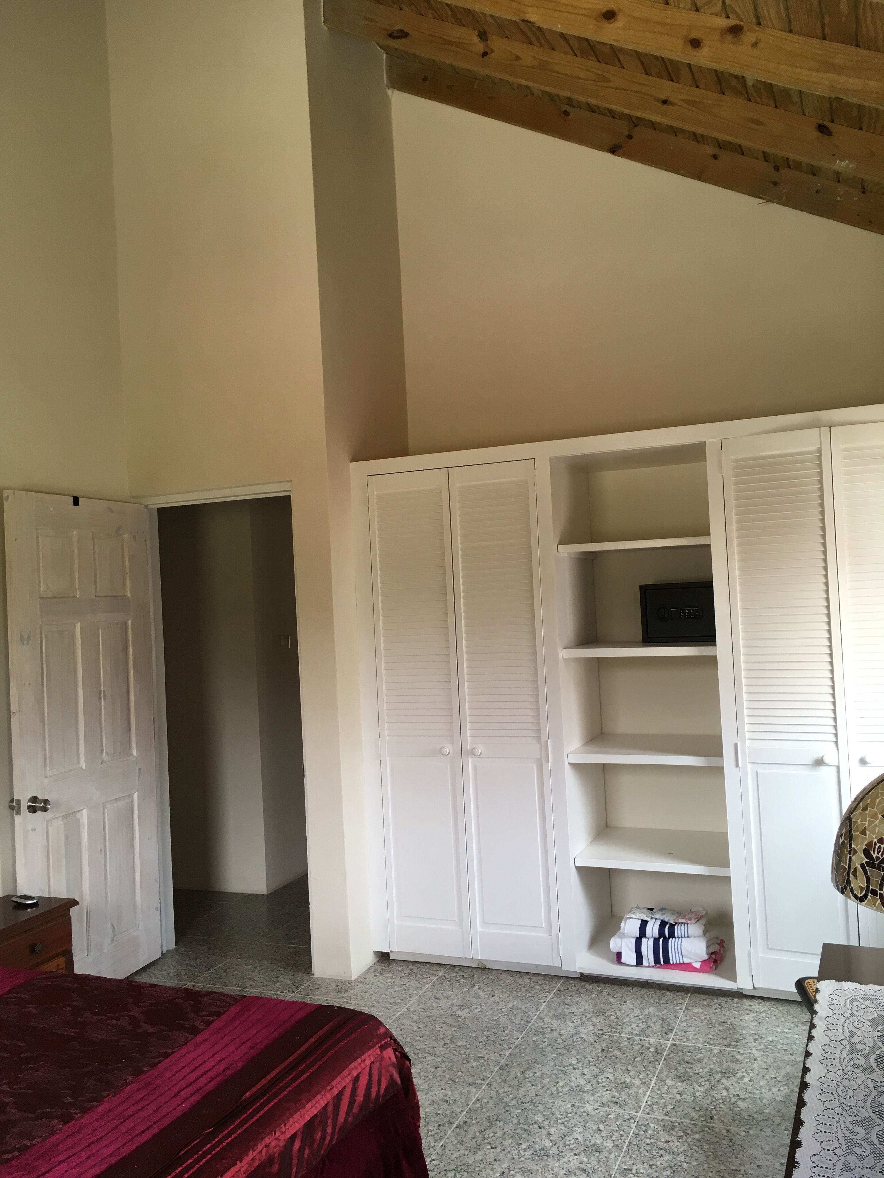 A bedroom with white closet doors, shelves, and a safe.