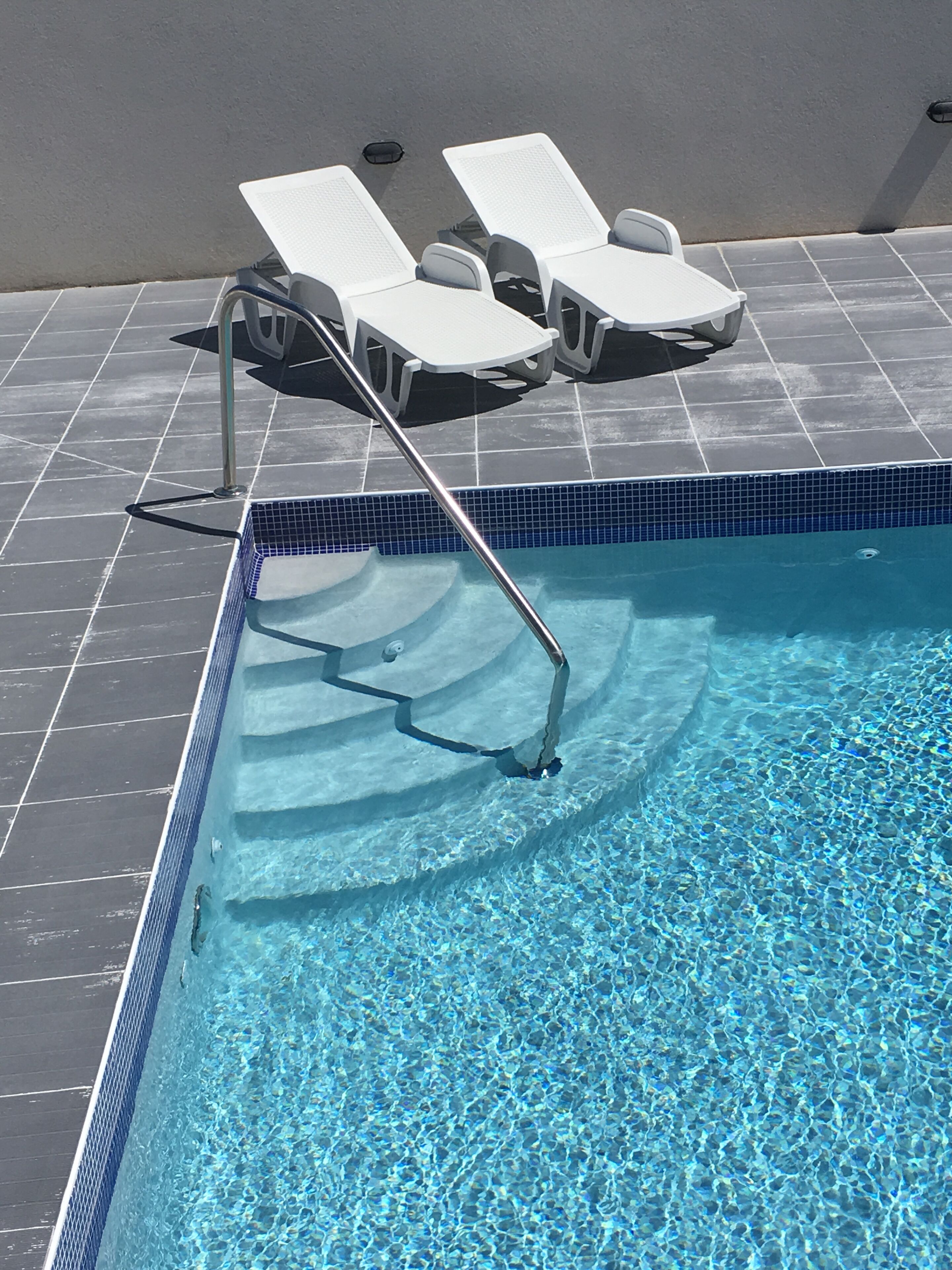 The pool steps with a metal handrail and two lounge chairs.