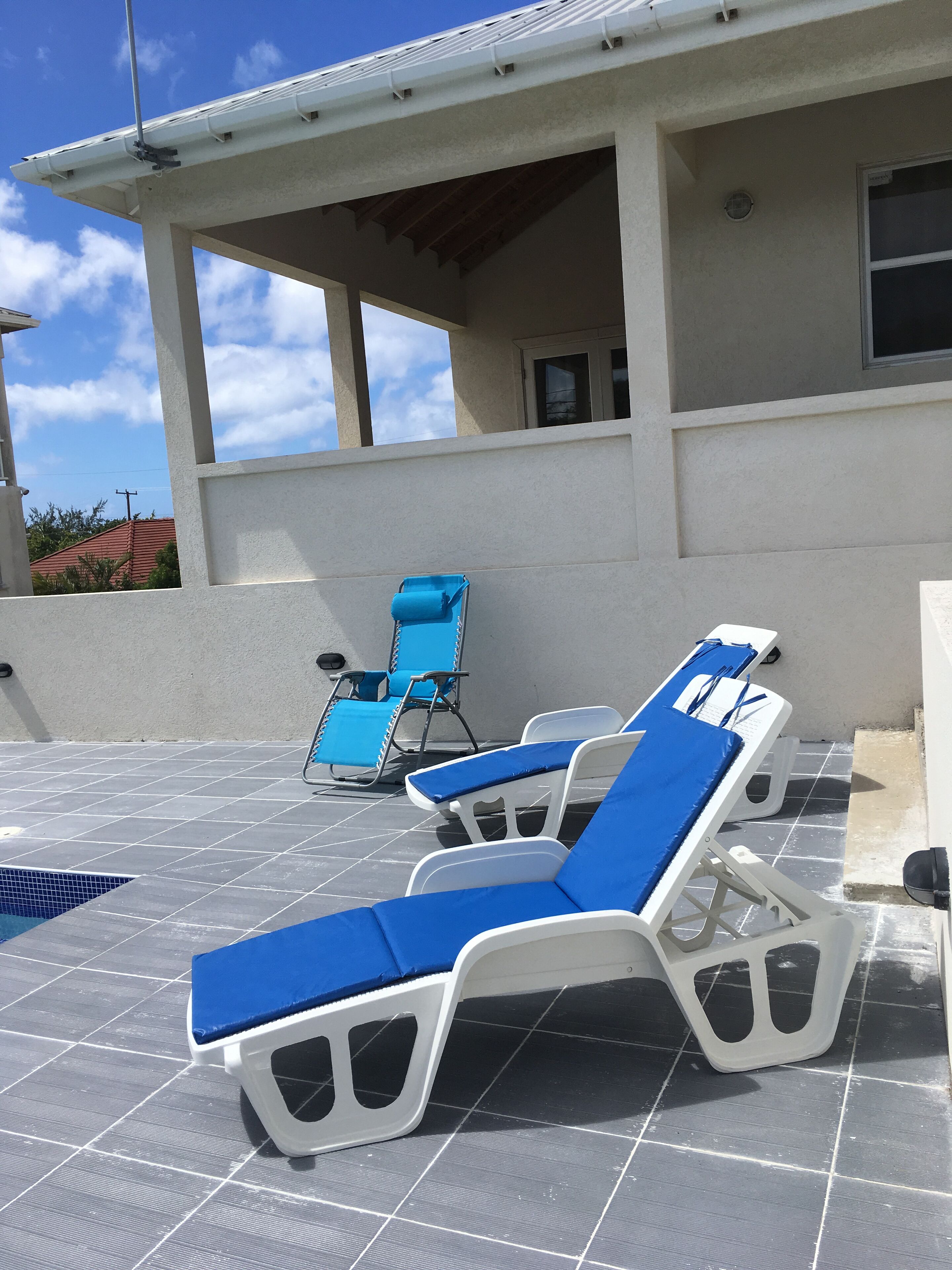 The pool terrace with lounge chairs and blue cushions.