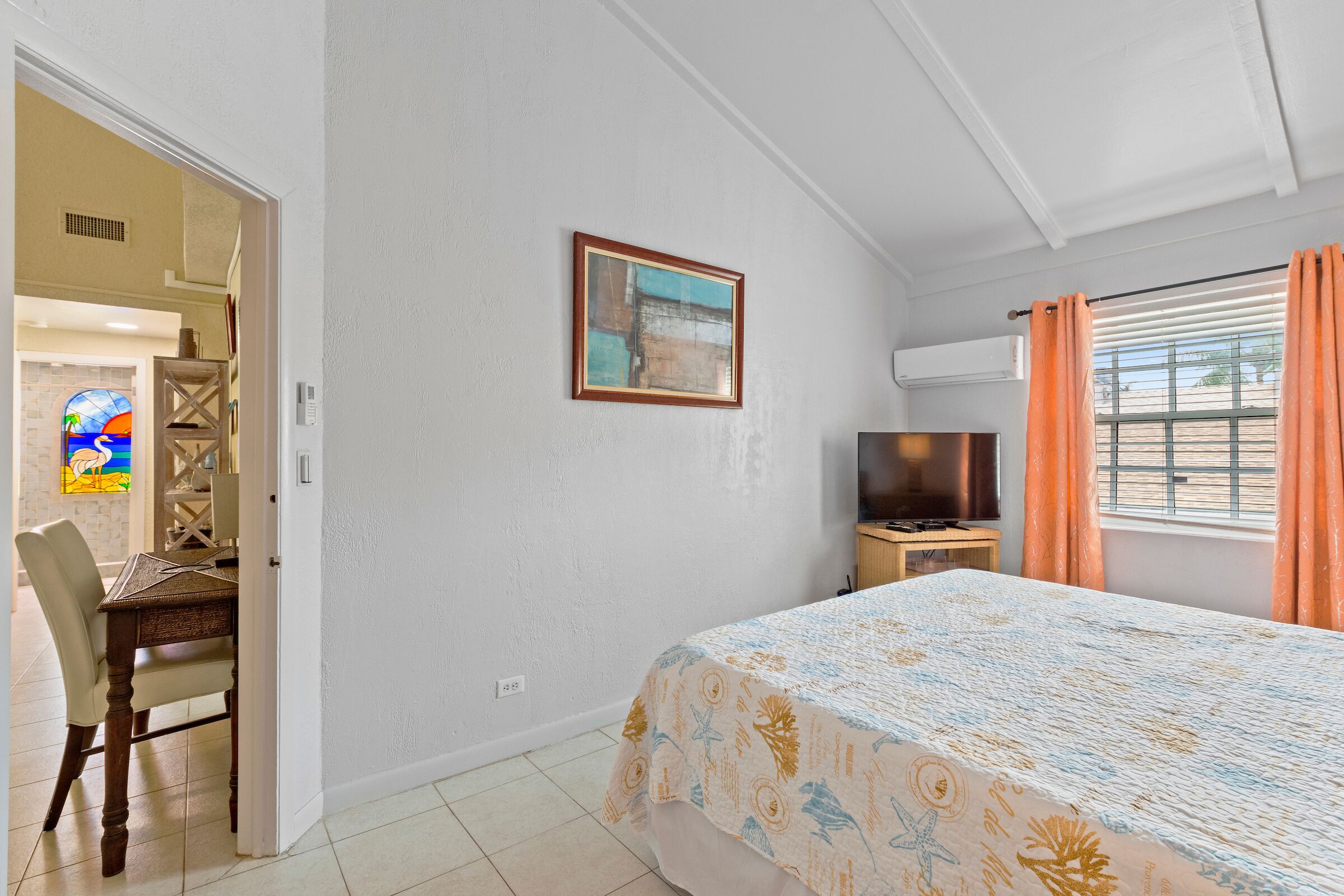 A bedroom with a quilted bedspread and orange curtains.