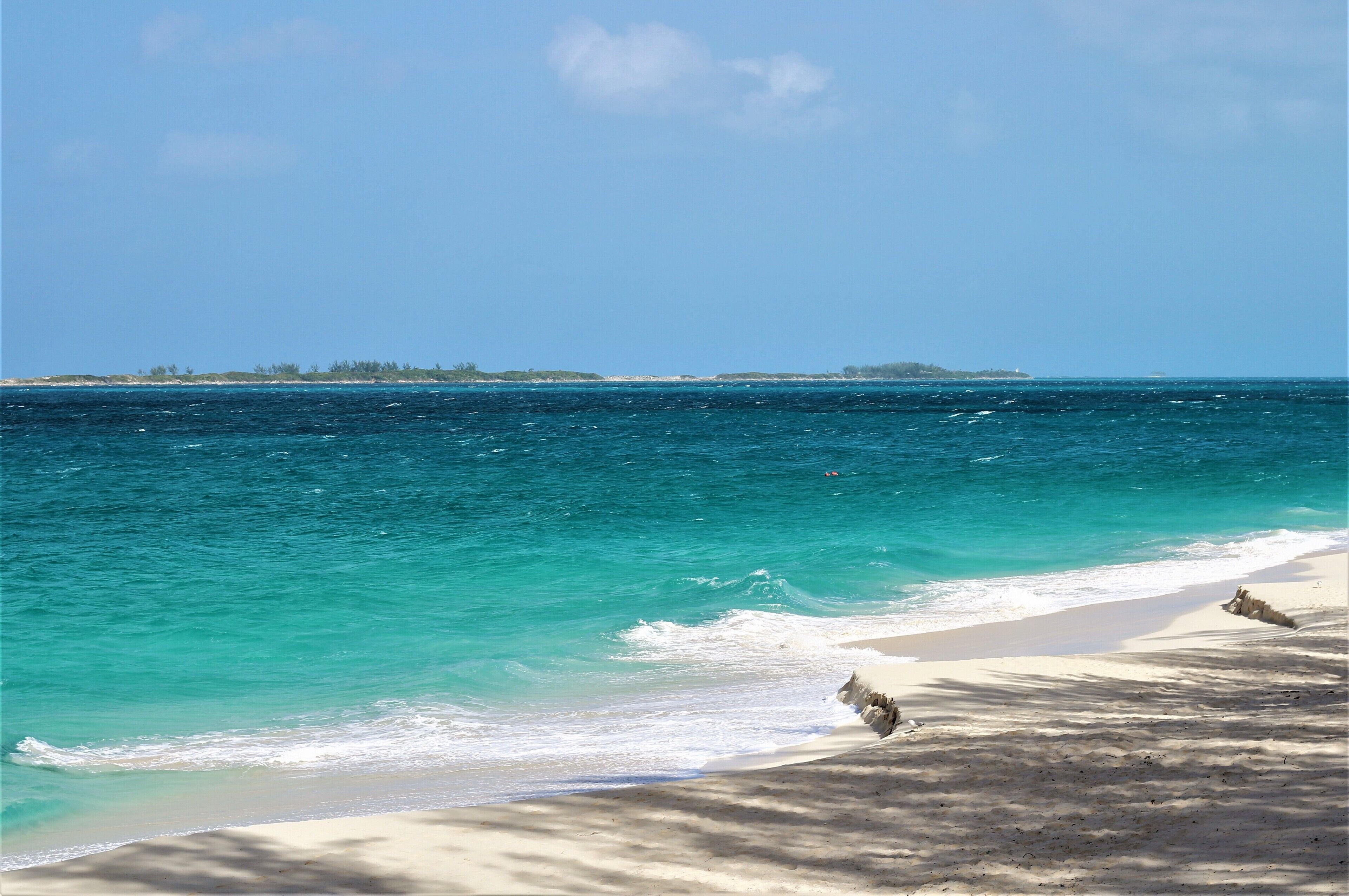 The beach and the turquoise sea, with a small island on the horizon.