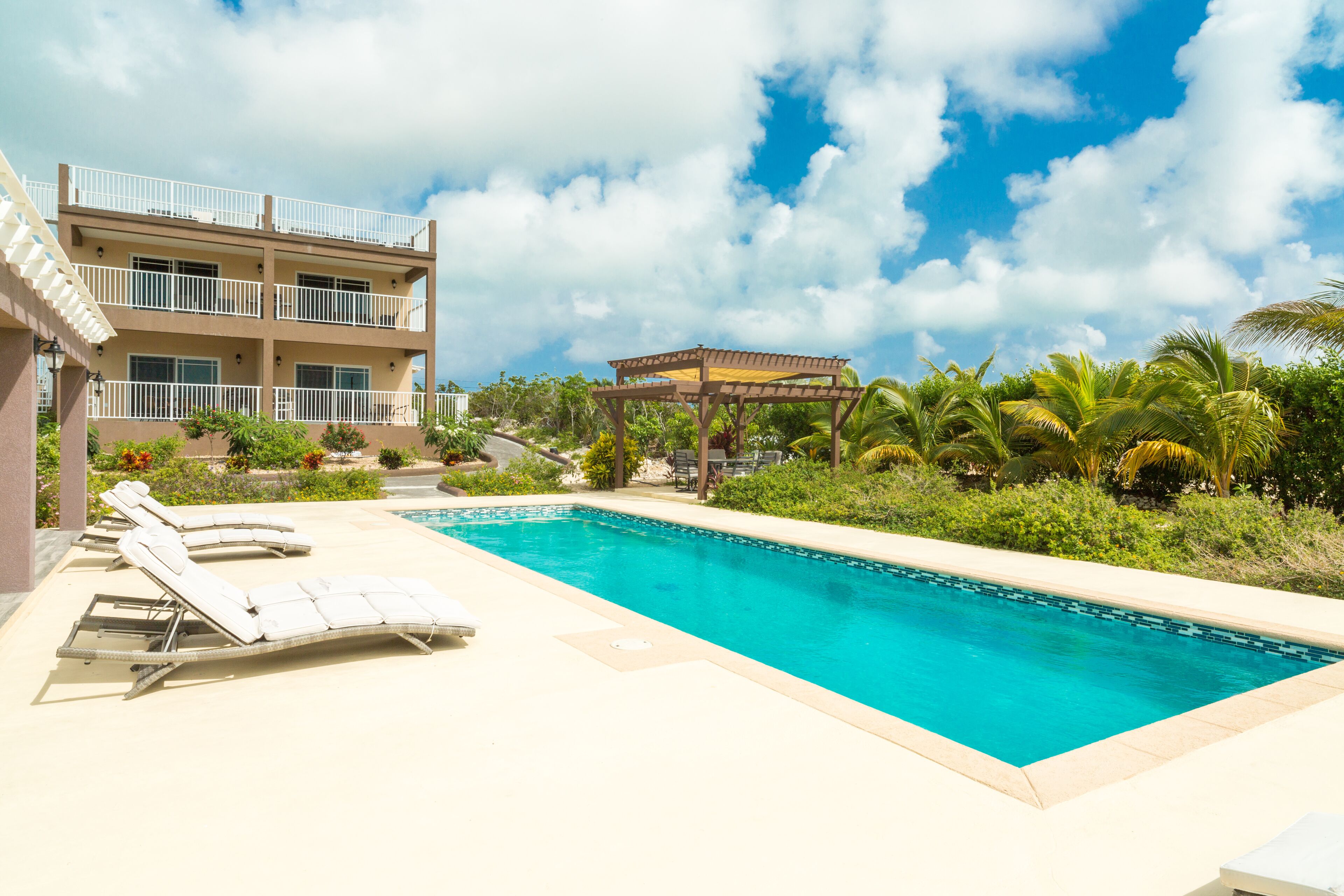 The pool with loungers, a pergola, and the house behind it.