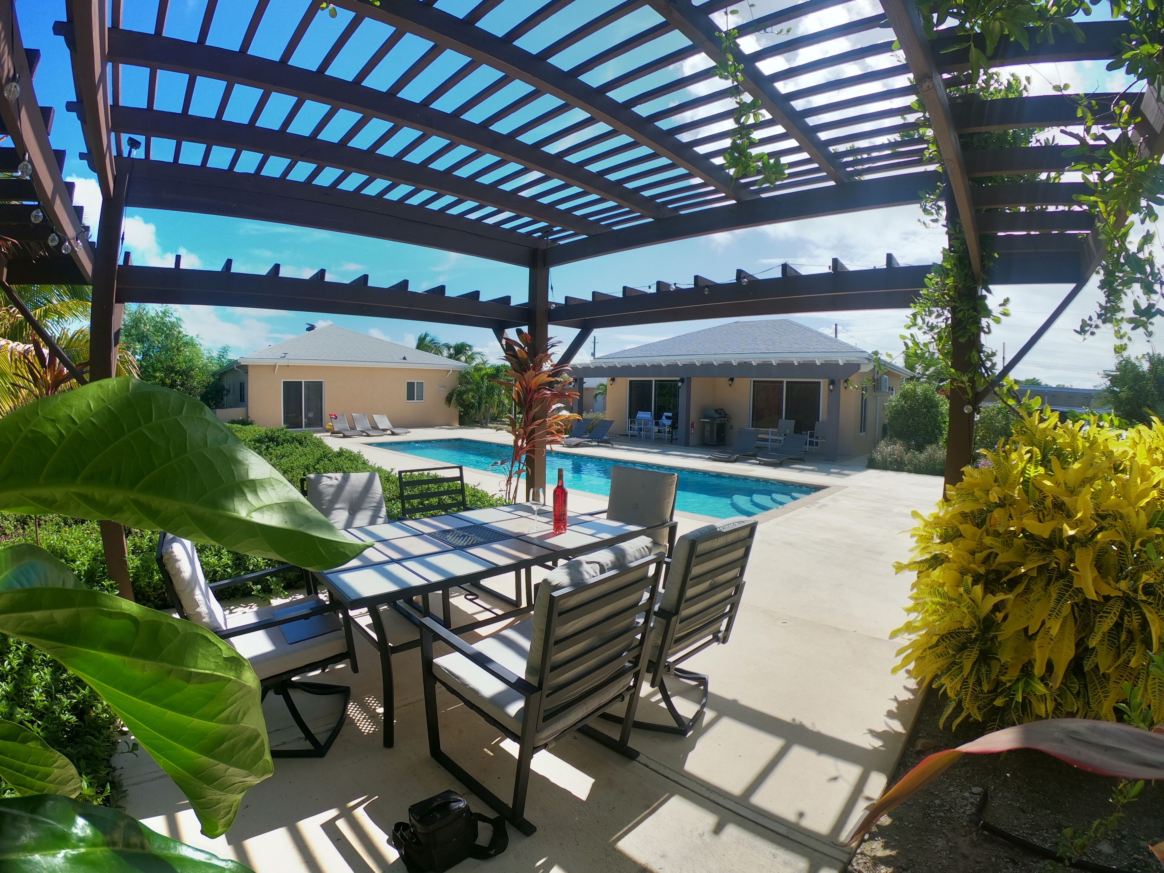 A dining table and chairs under a pergola next to the pool.
