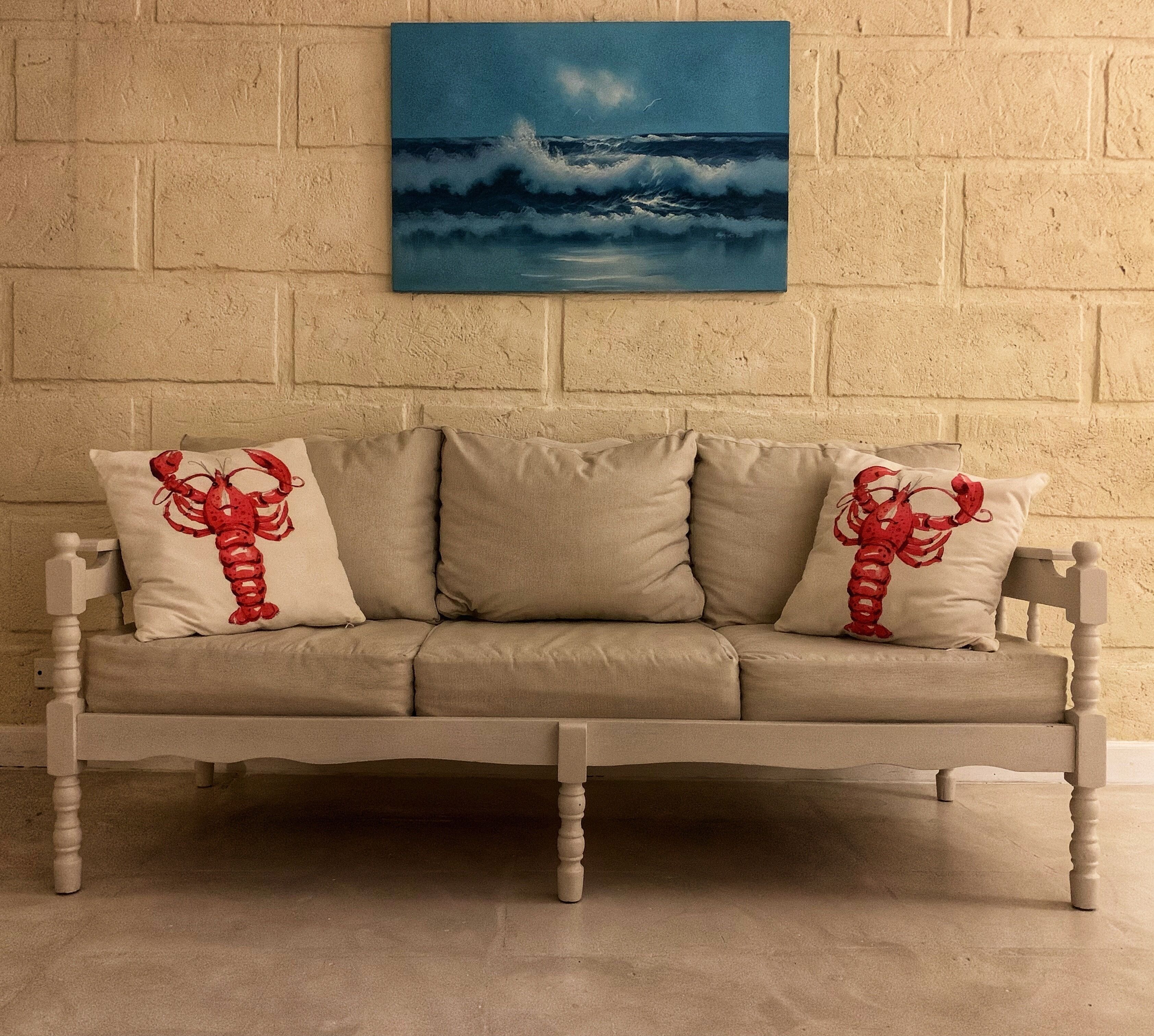 A wooden seat with cushions, below a sea painting.