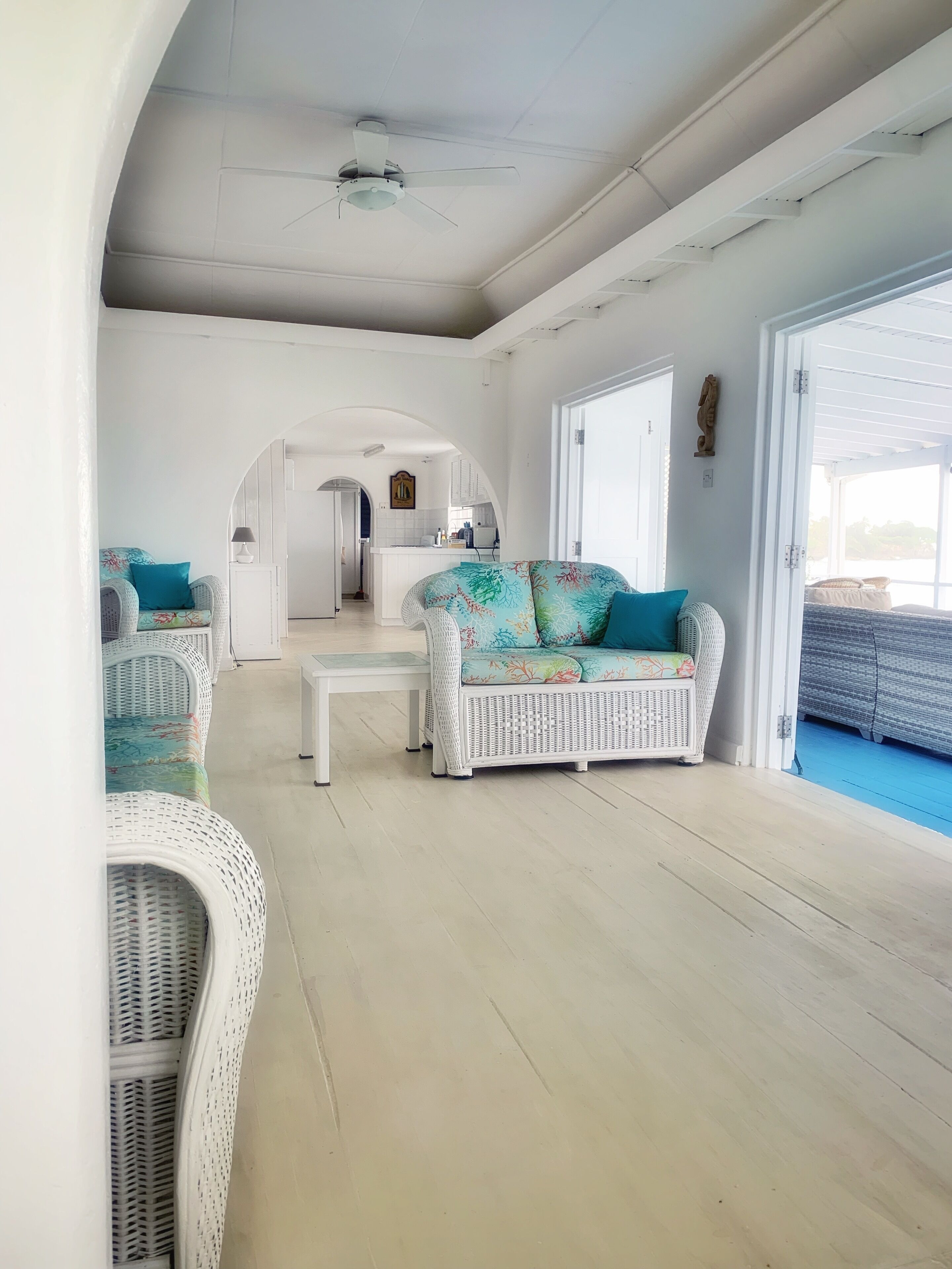 The living room with white wicker seats, with the kitchen beyond.