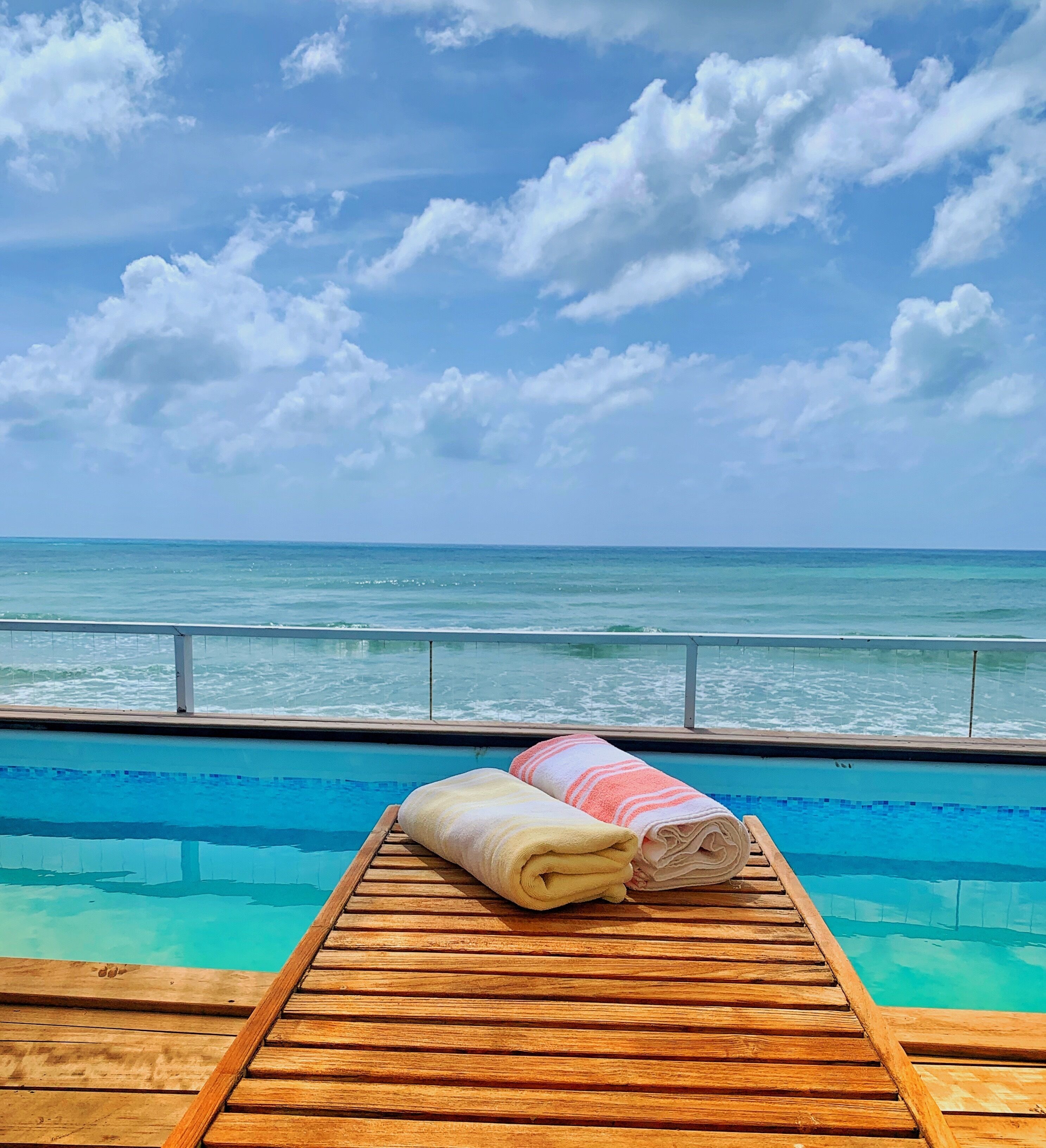 Two towels on a lounger next to the pool, with a sea view.