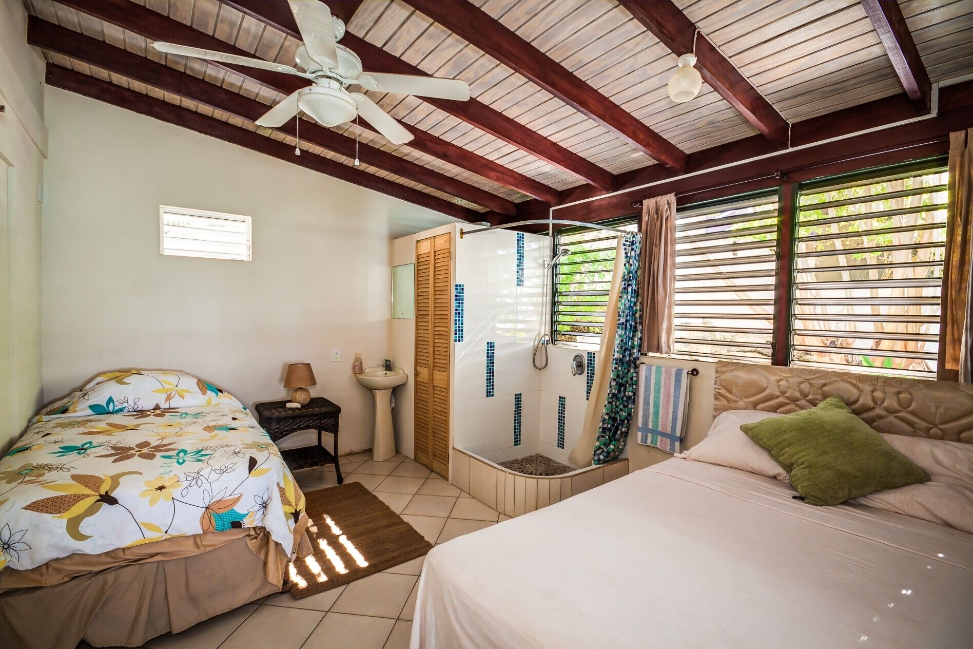 A room with two beds, a corner shower, and a sink.