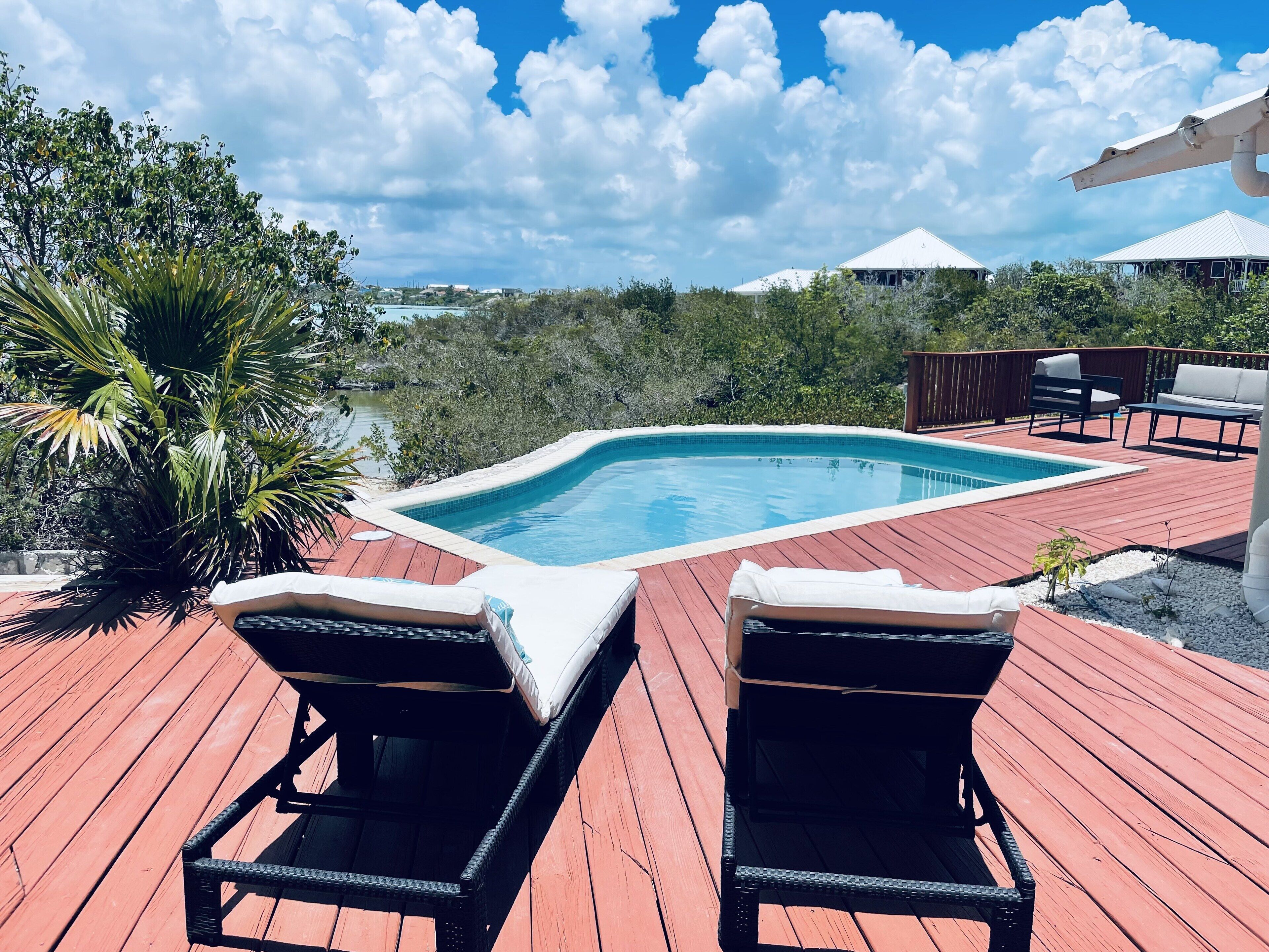Two loungers on a red wood deck next to the pool.