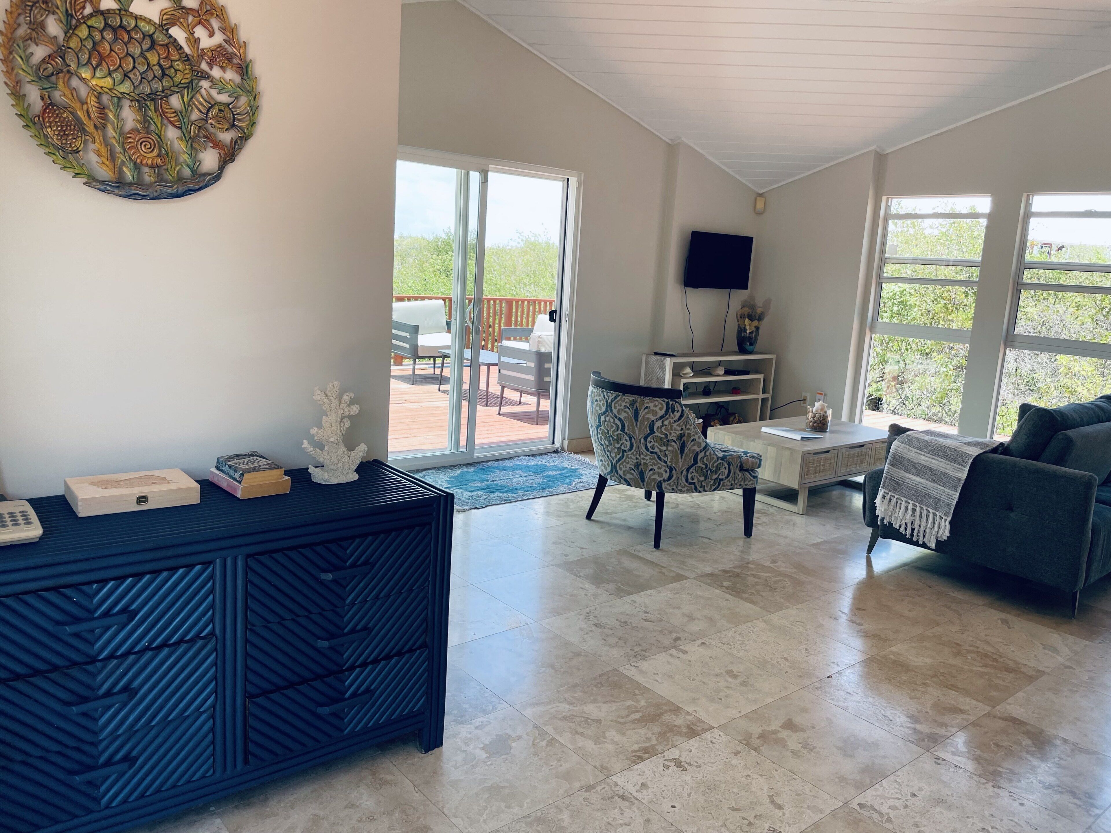 A living room with a blue chest of drawers and a glass door to the deck.
