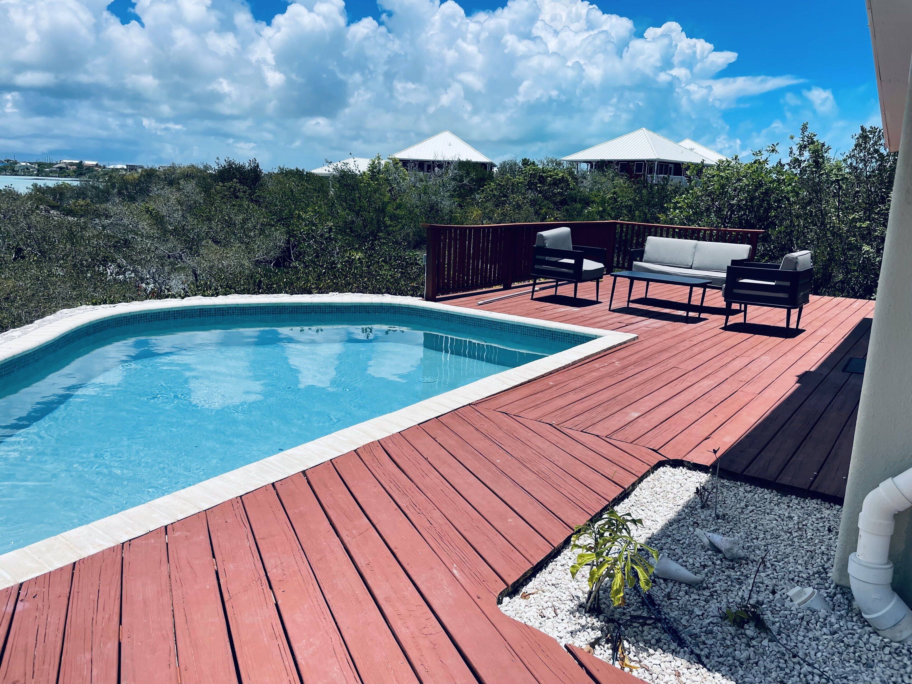 The pool and the deck with outdoor seats and a low table.