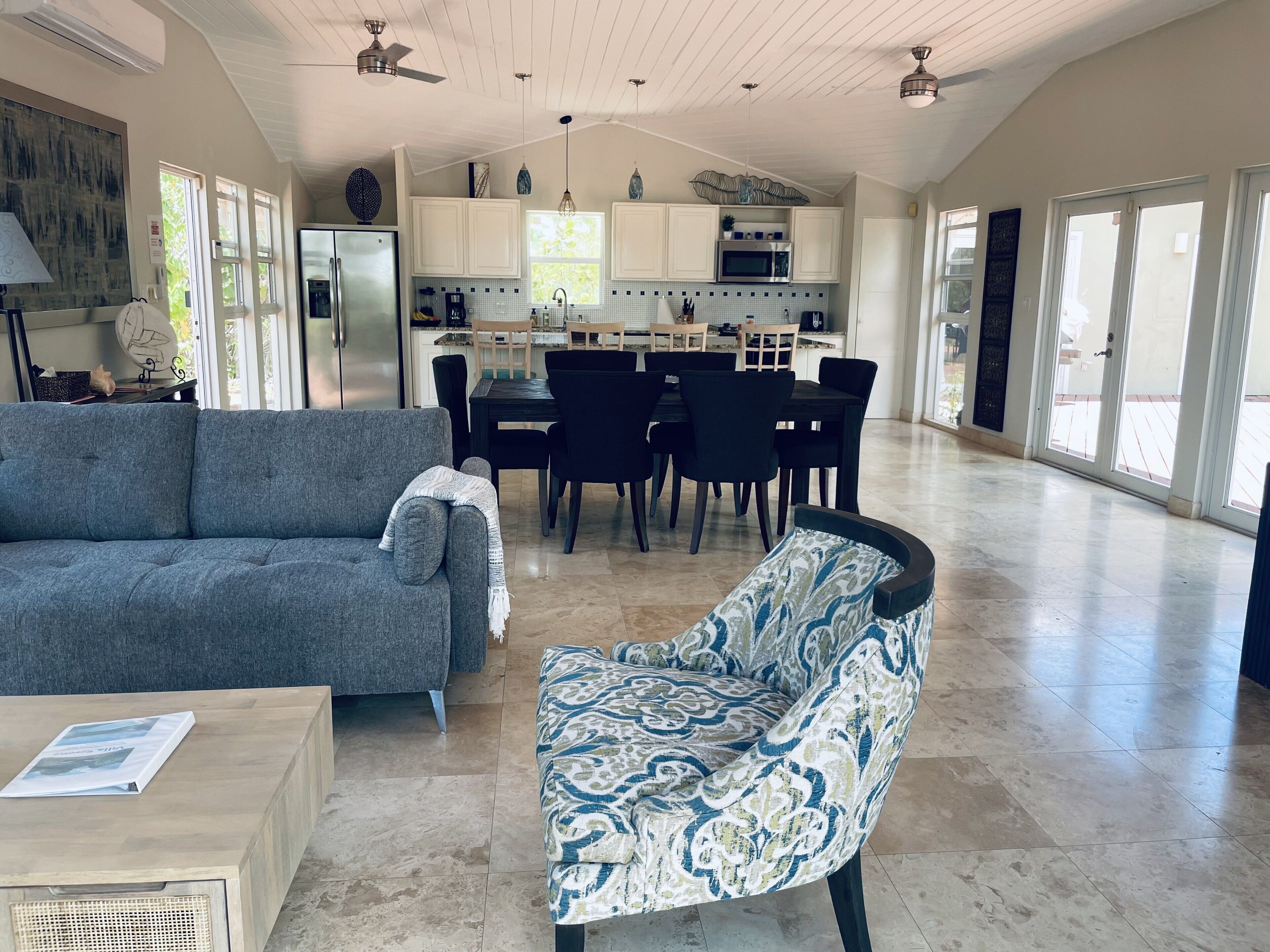 A living room with a gray sofa, a dining table, and the kitchen behind.