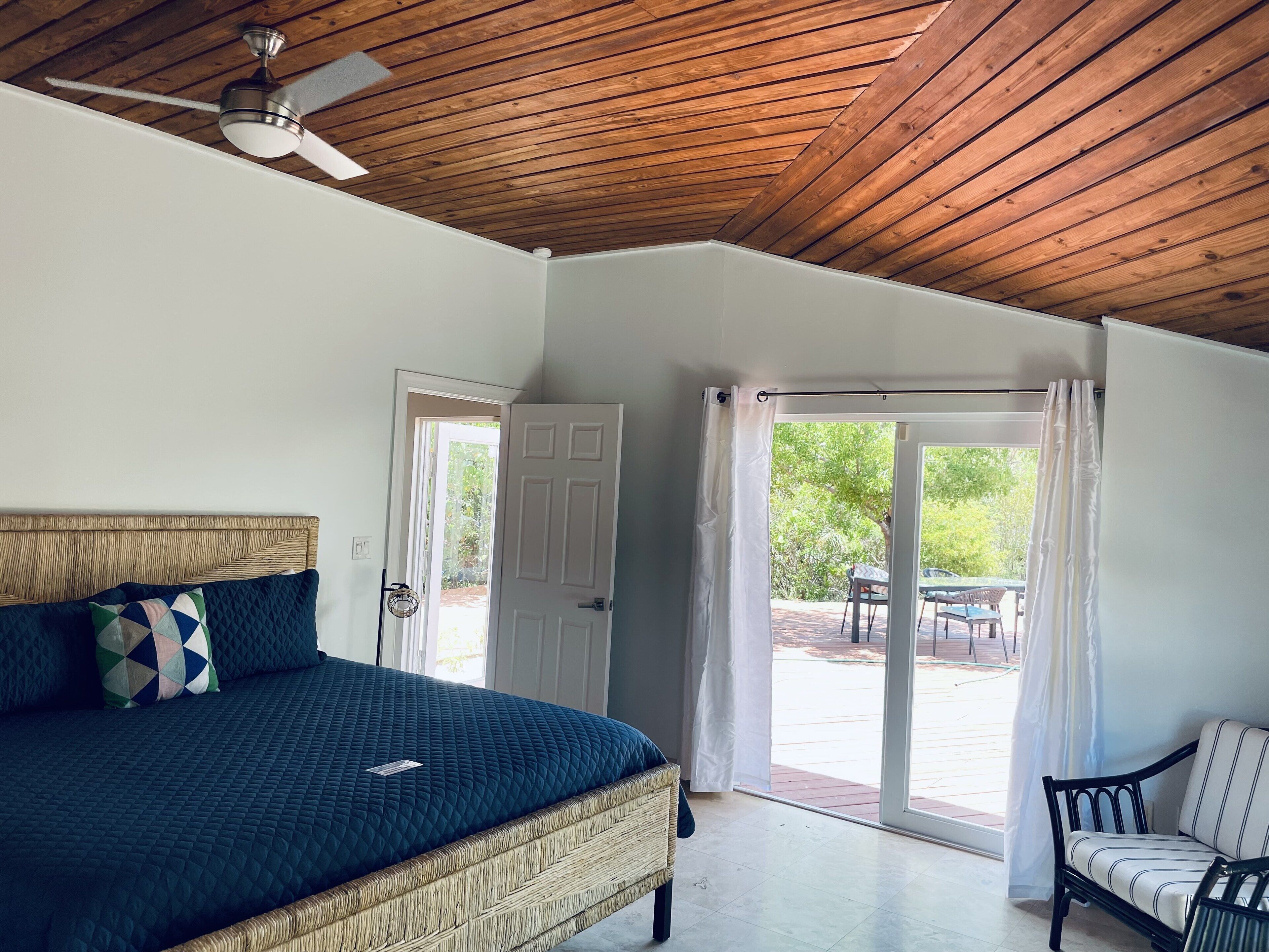 A bedroom with a bed with a blue cover and a glass door to the deck.