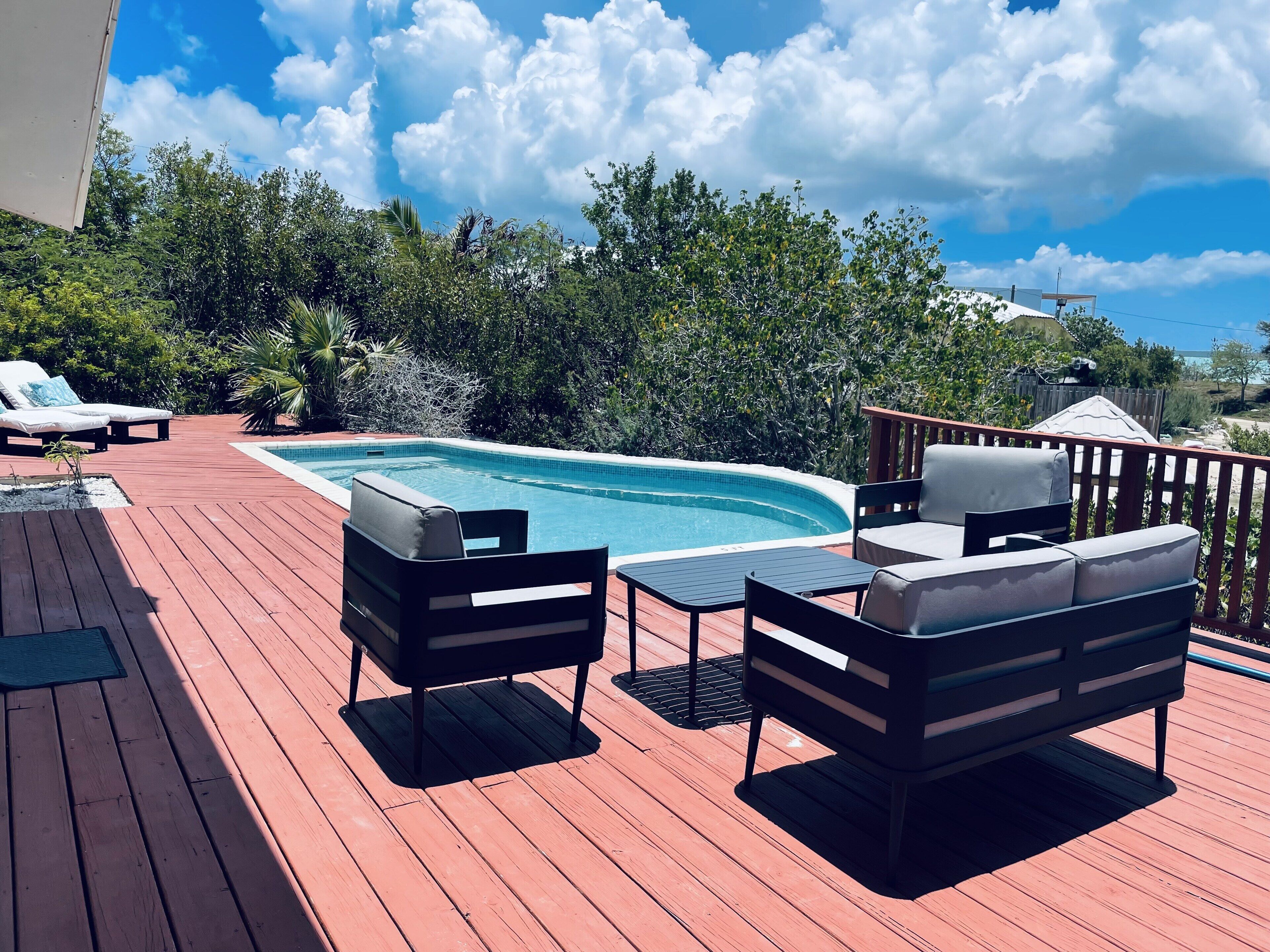 Outdoor seats and a low table on the deck next to the pool.