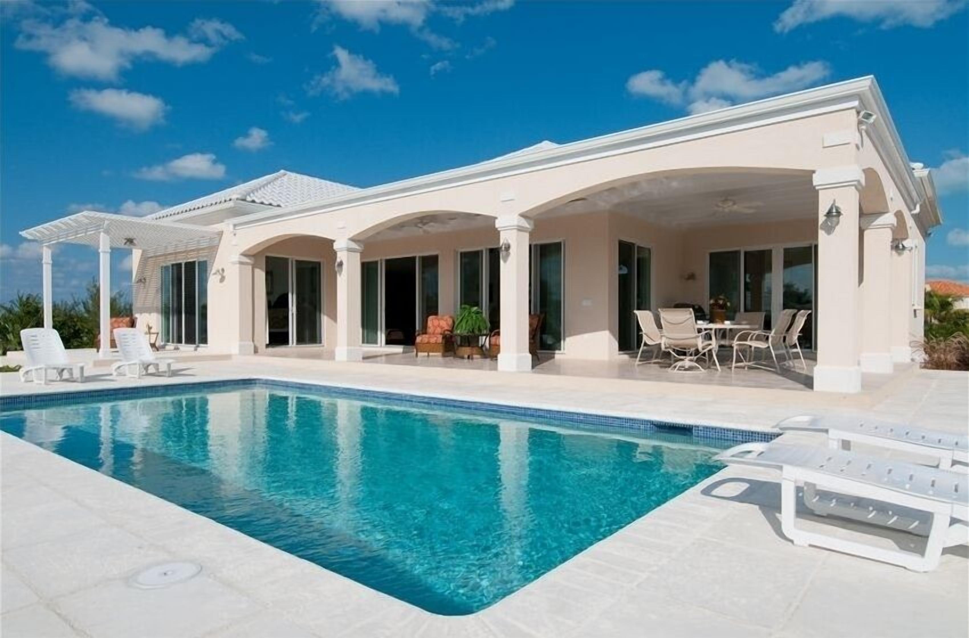 The villa with a covered terrace and the pool under a blue sky.