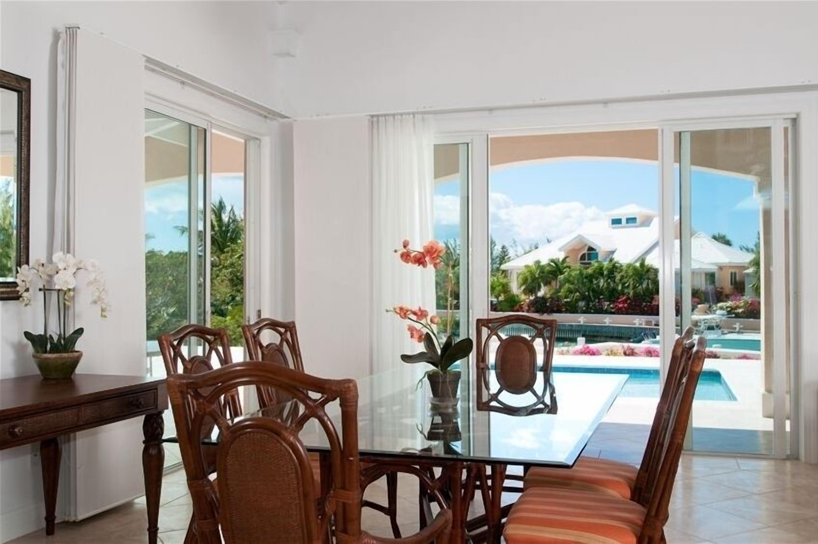 A dining room with a glass table and a view of the pool.