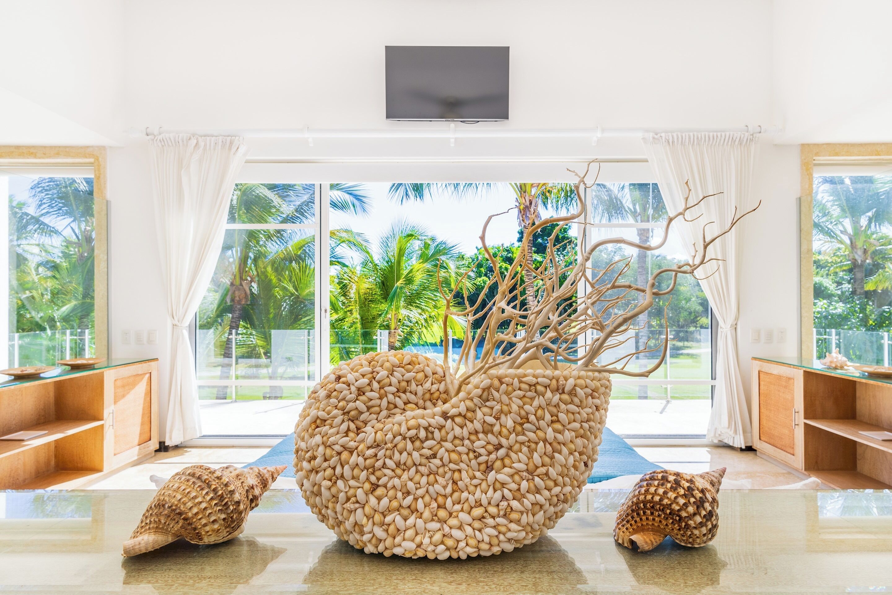 A shell sculpture and two conch shells stand on a glass table in front of the glass doors.