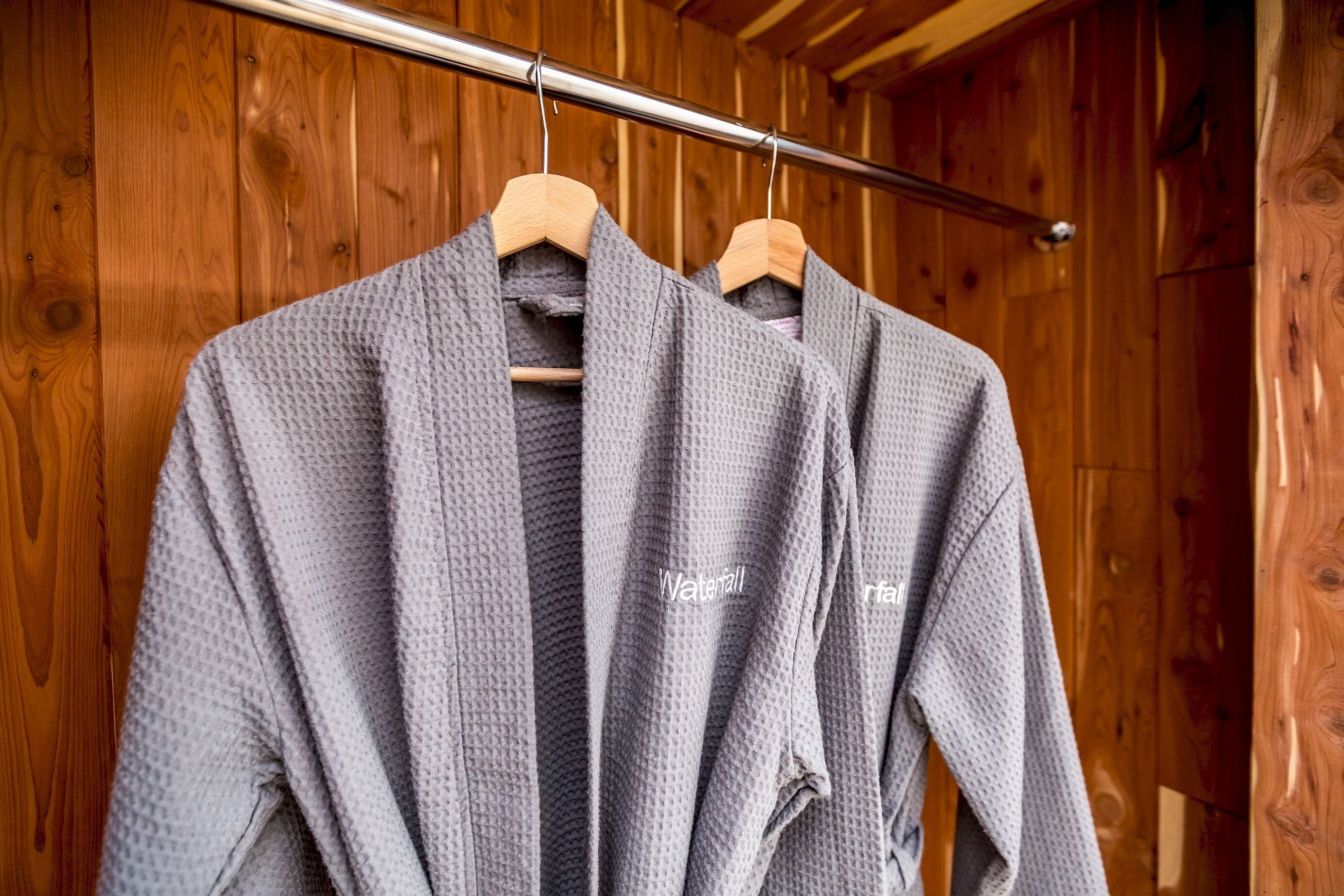 Two gray robes with the villa name hang in a wooden closet.