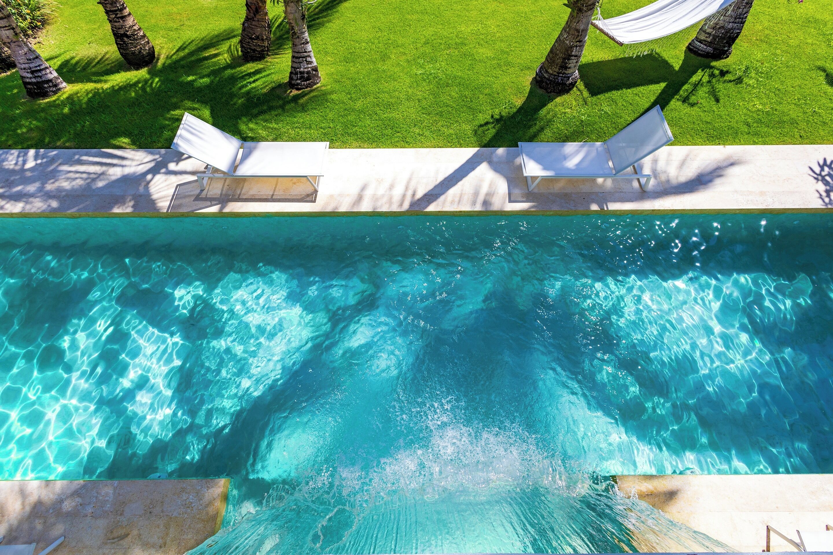 The view from above shows the pool, two sun loungers, and the lawn with palm trees.