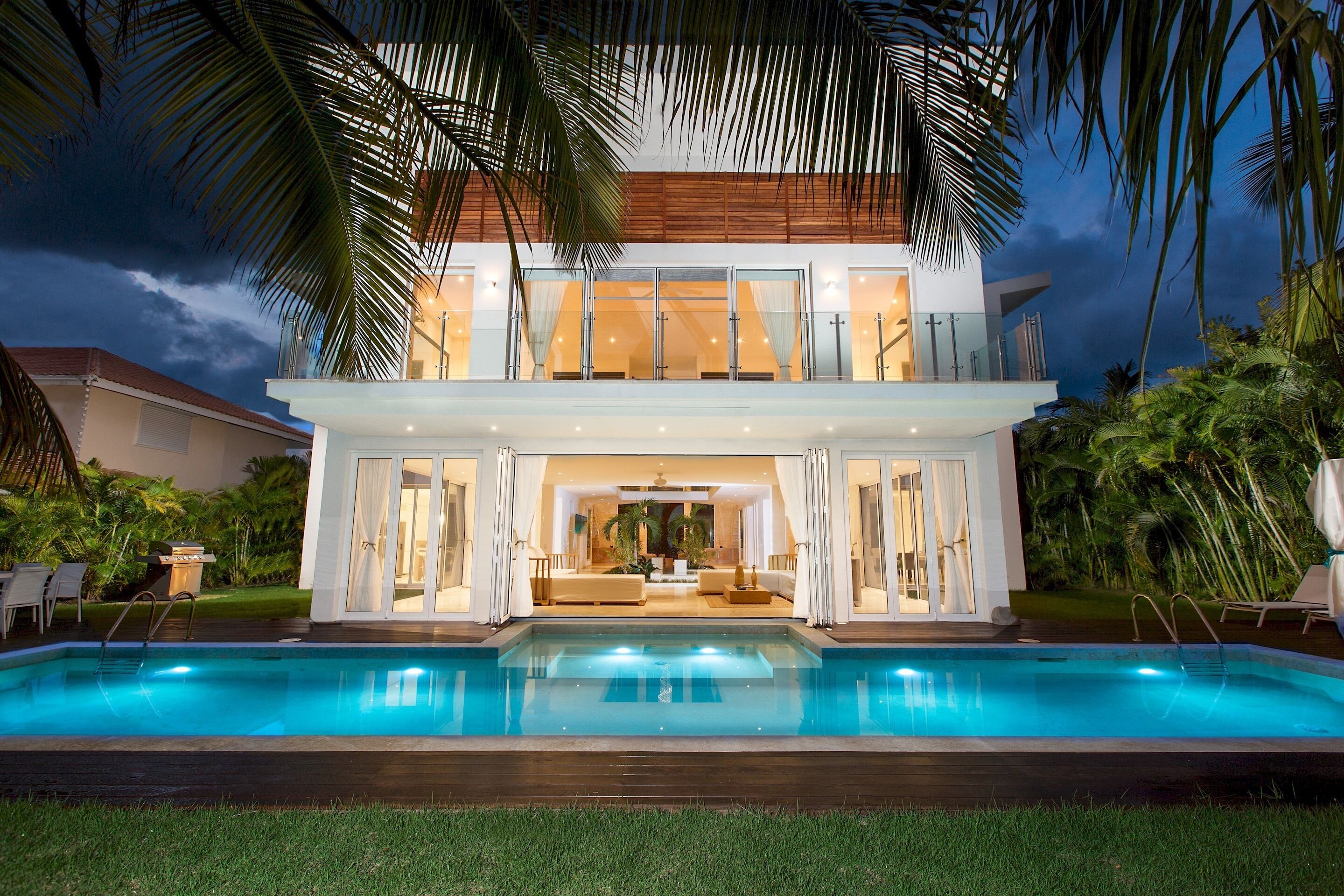 The pool reflects the lights of the two-story villa at dusk.