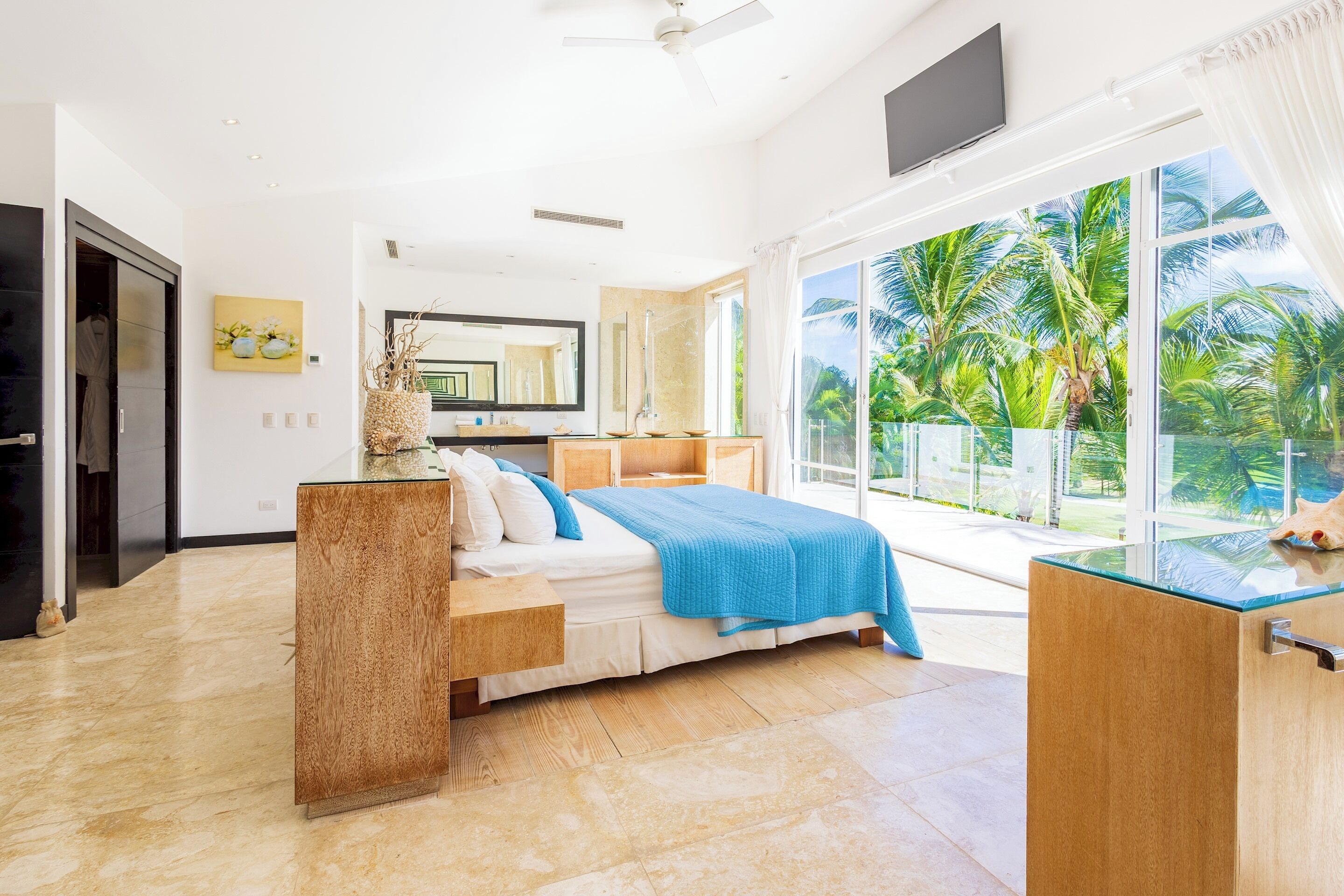 The bedroom has a bed with a blue cover, a wooden headboard unit, and glass doors to a terrace.