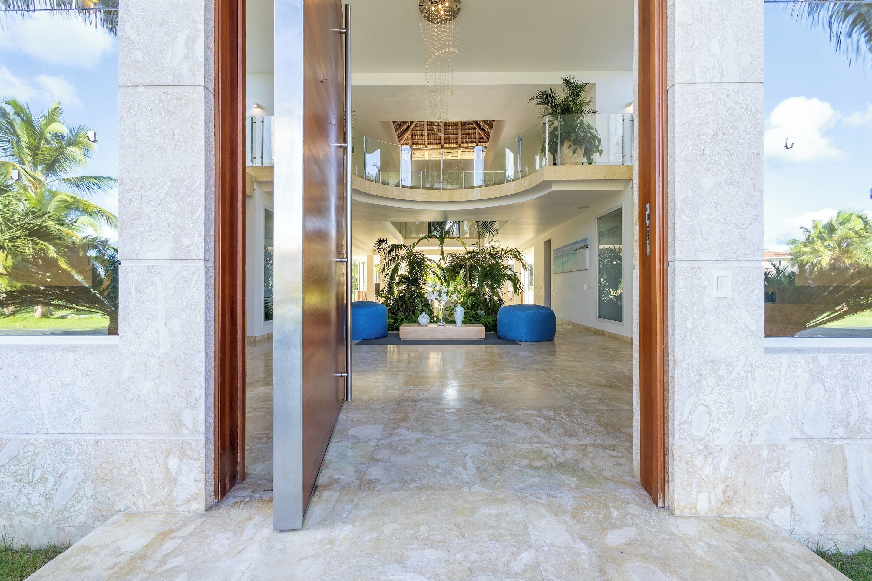 The open front door shows the two-story hall with plants and a chandelier.