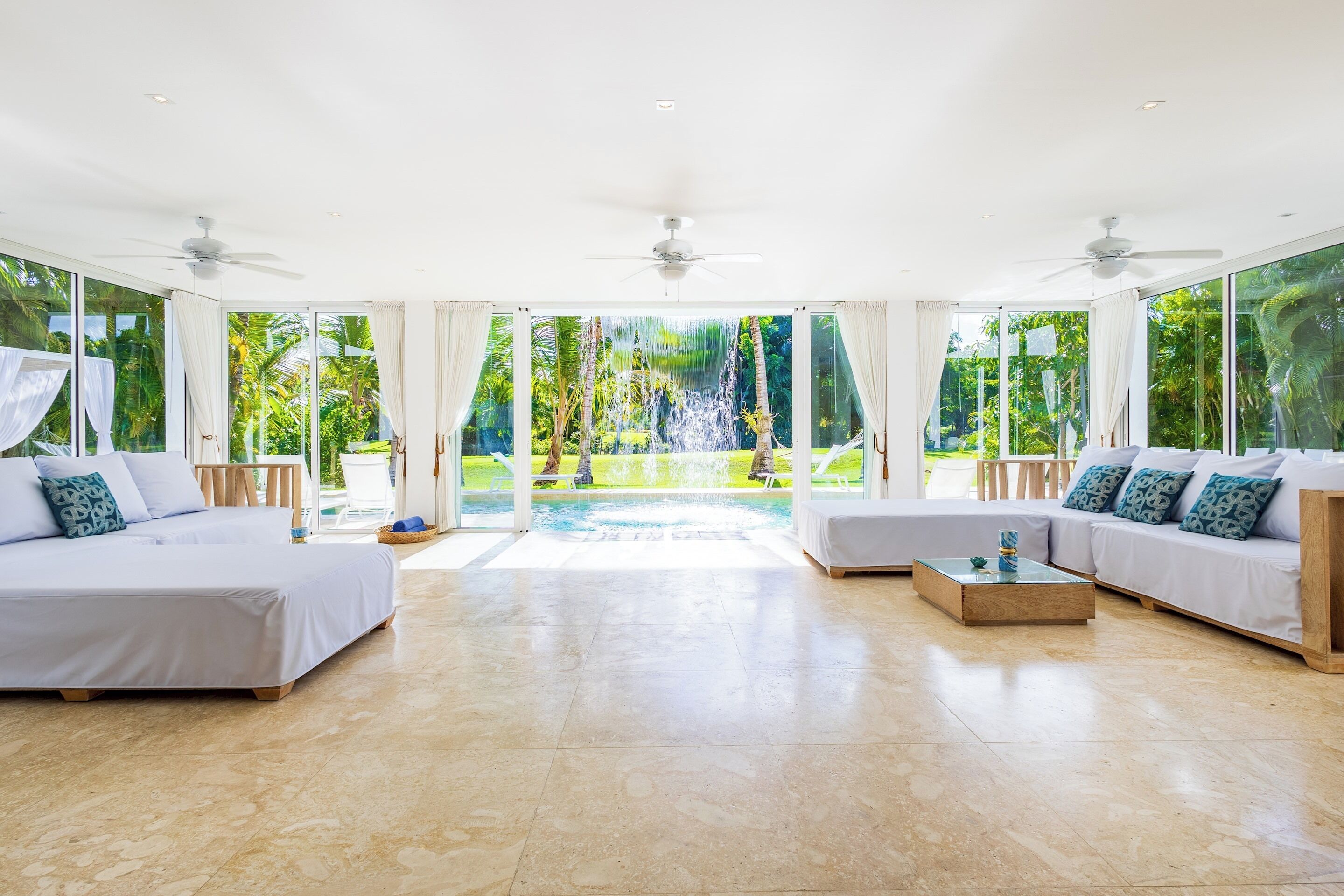 The living room has white sofas on both sides and open doors with a view of the pool waterfall.