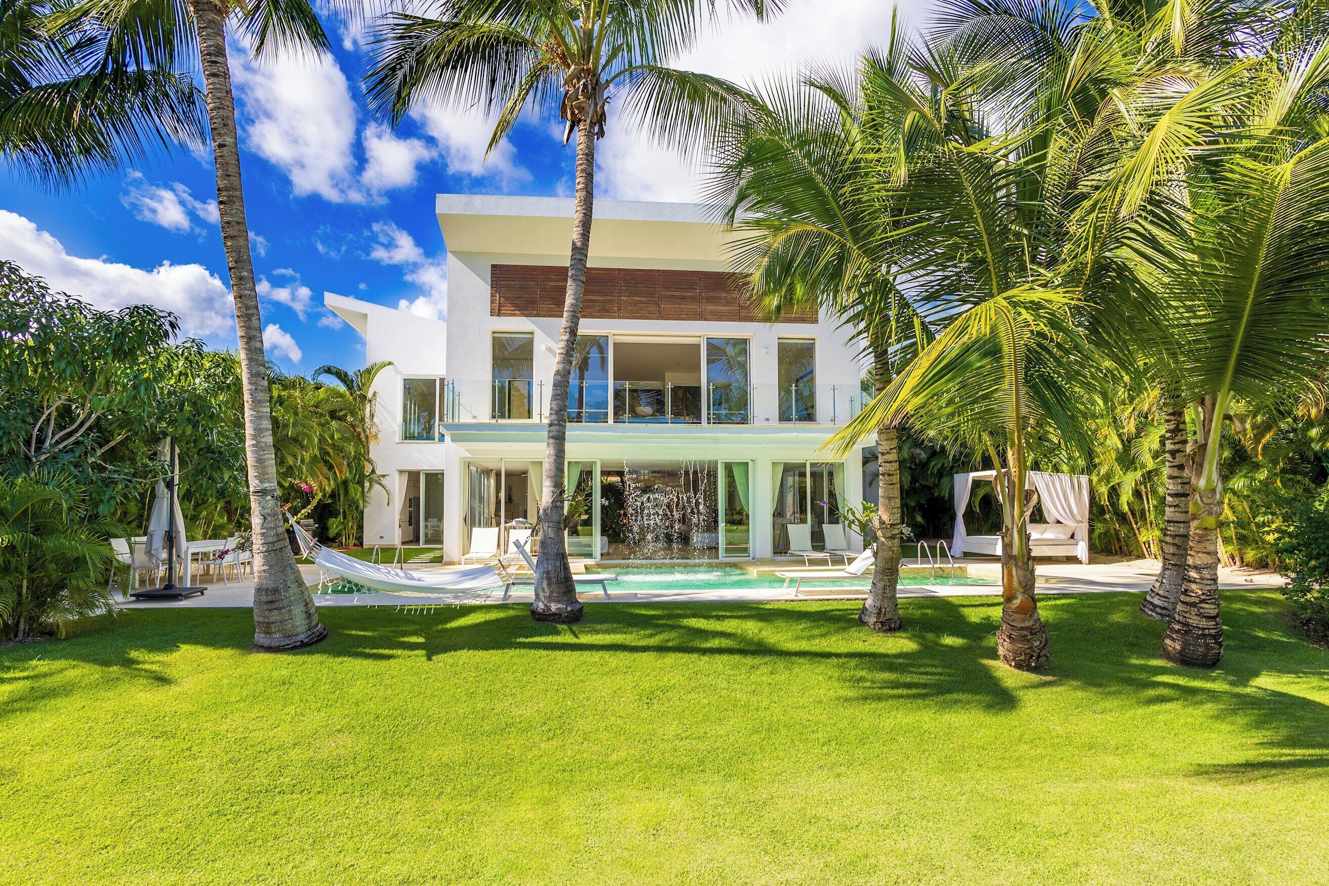 The two-story villa stands behind the pool, the waterfall, a hammock, and the lawn.