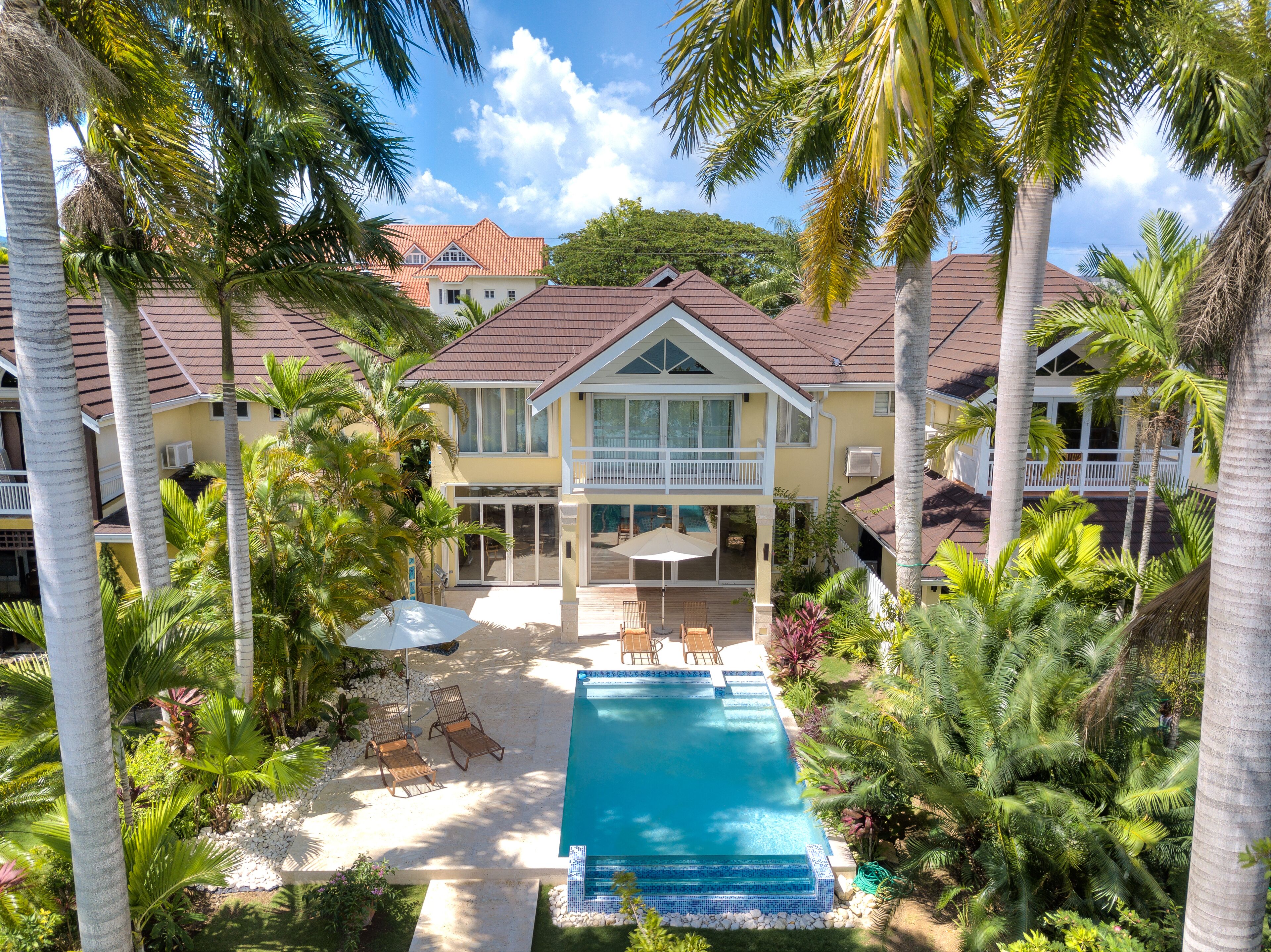 An aerial view of the villa with the pool, sun loungers, and palm trees.
