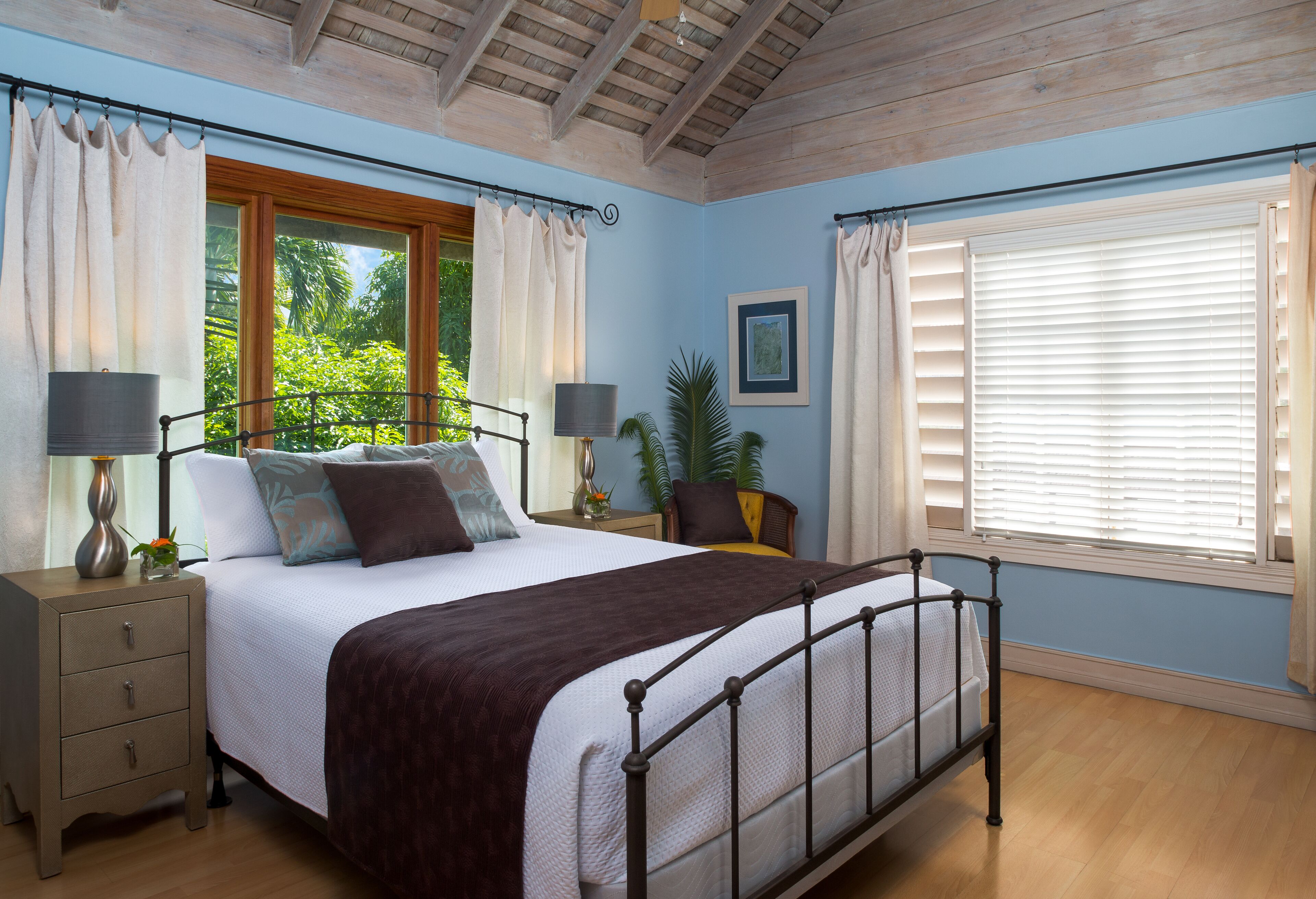 A bedroom with a double bed, blue walls, and two windows.