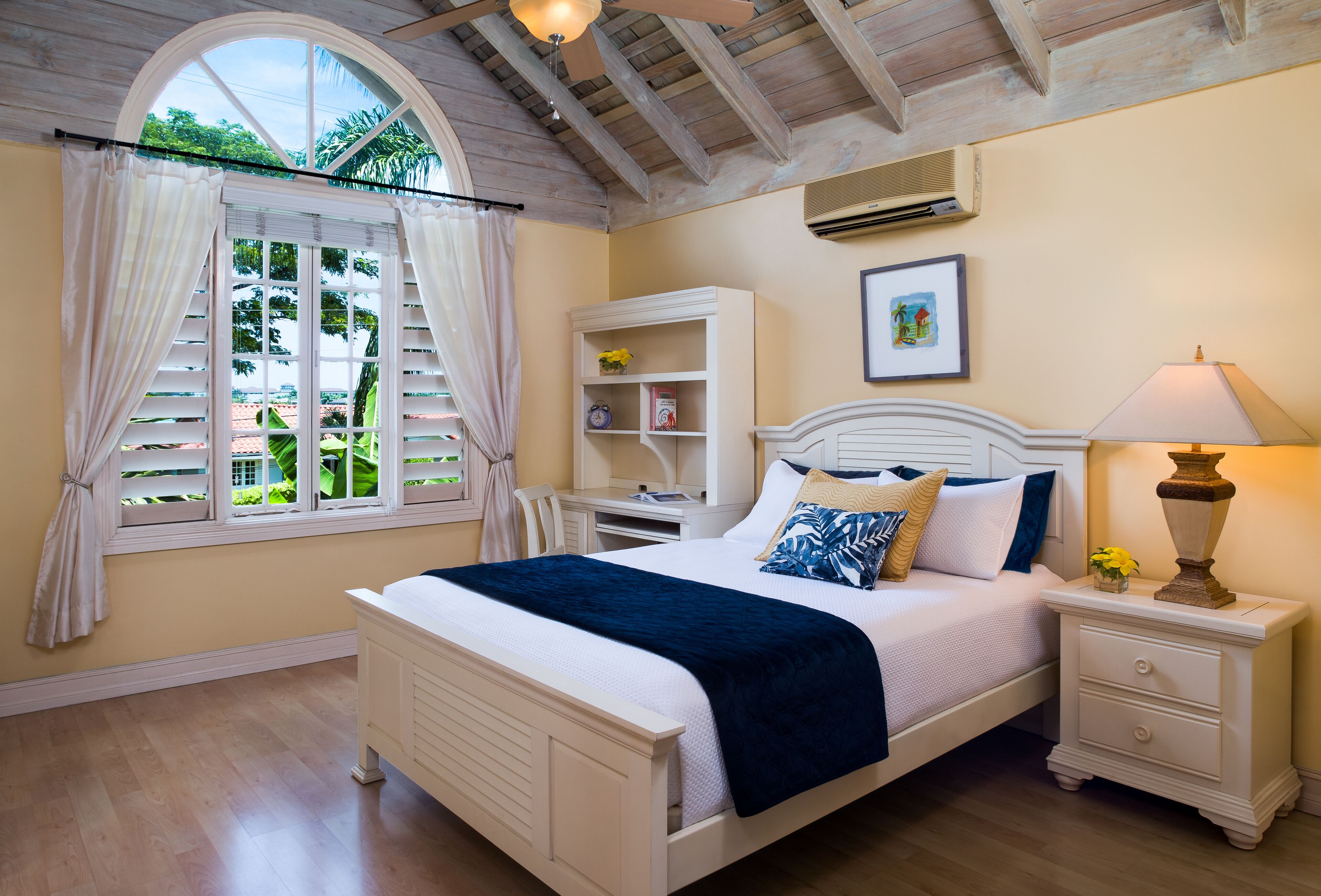 A bedroom with a double bed, a desk, and an arched window.