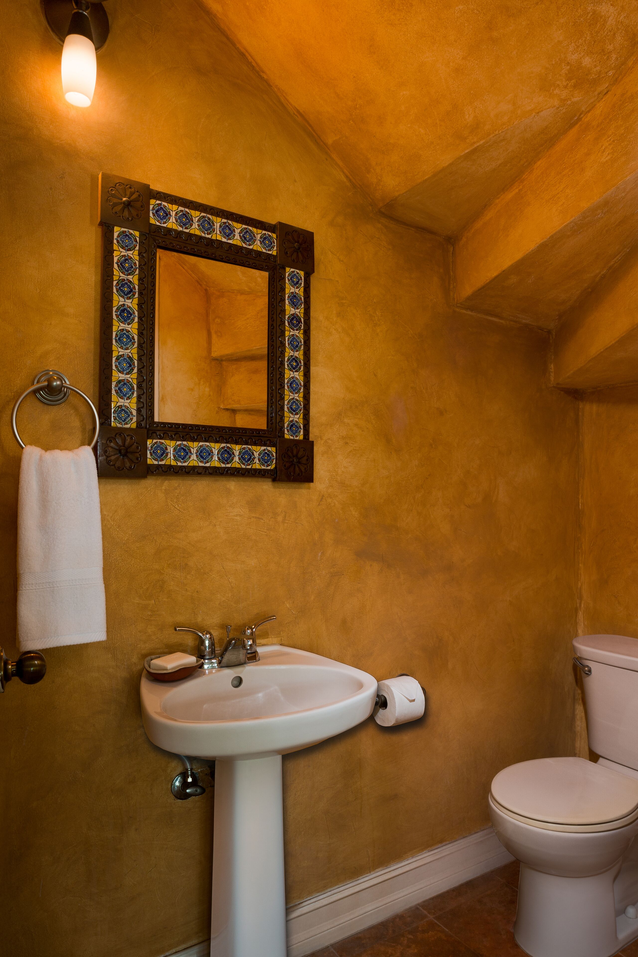 A bathroom with a pedestal sink, a toilet, and a framed mirror.